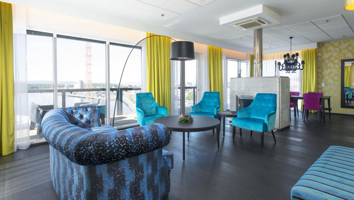 Suite interior with blue armchairs and sofa, coffee table, green curtains and a nice view from the panoramic windows.