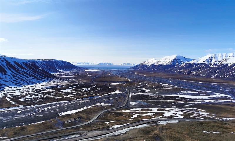 Landskap som er noe dekket i snø, snødekte fjell og dal med havet i horisonten