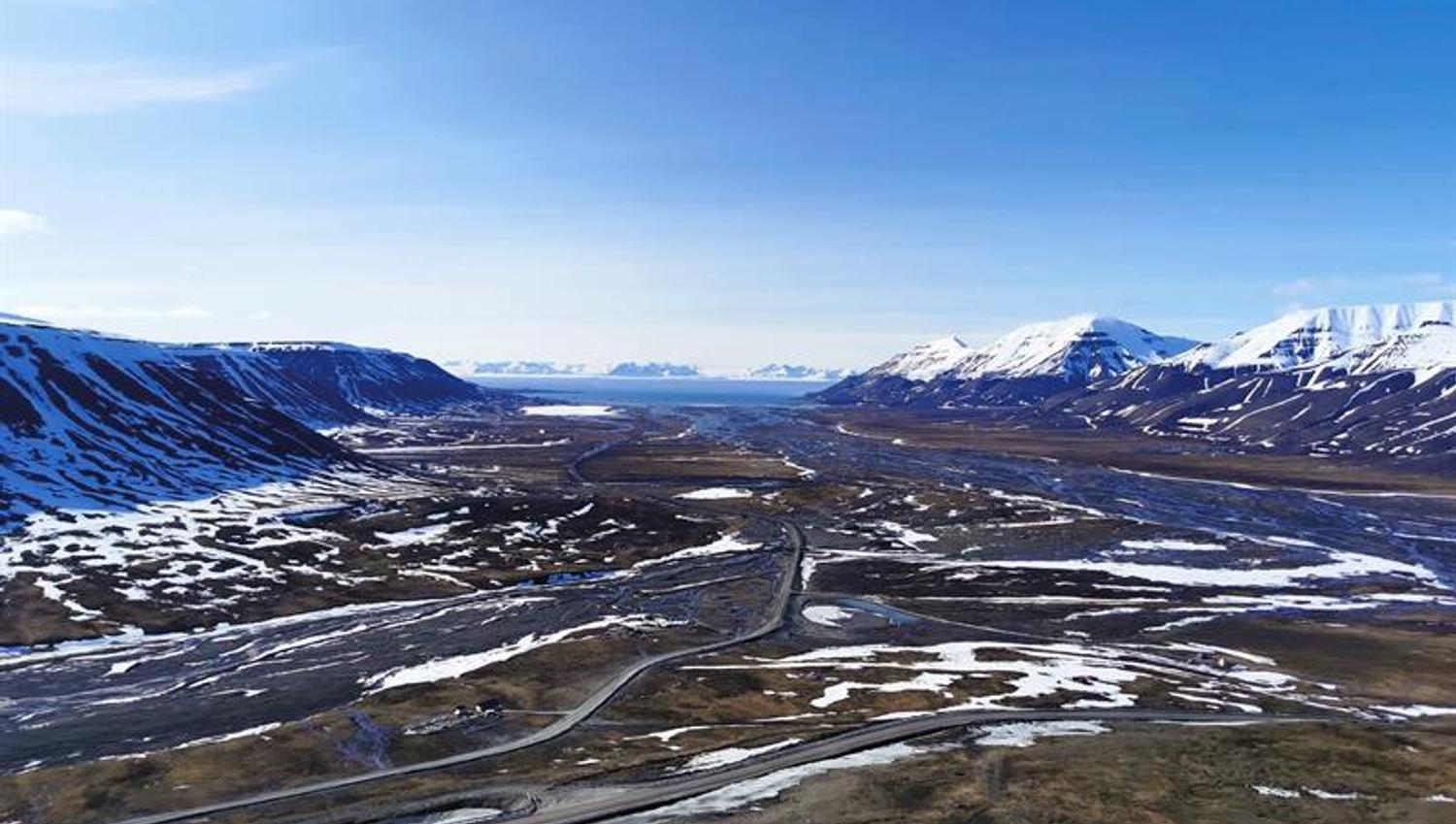 Landskap som er noe dekket i snø, snødekte fjell og dal med havet i horisonten