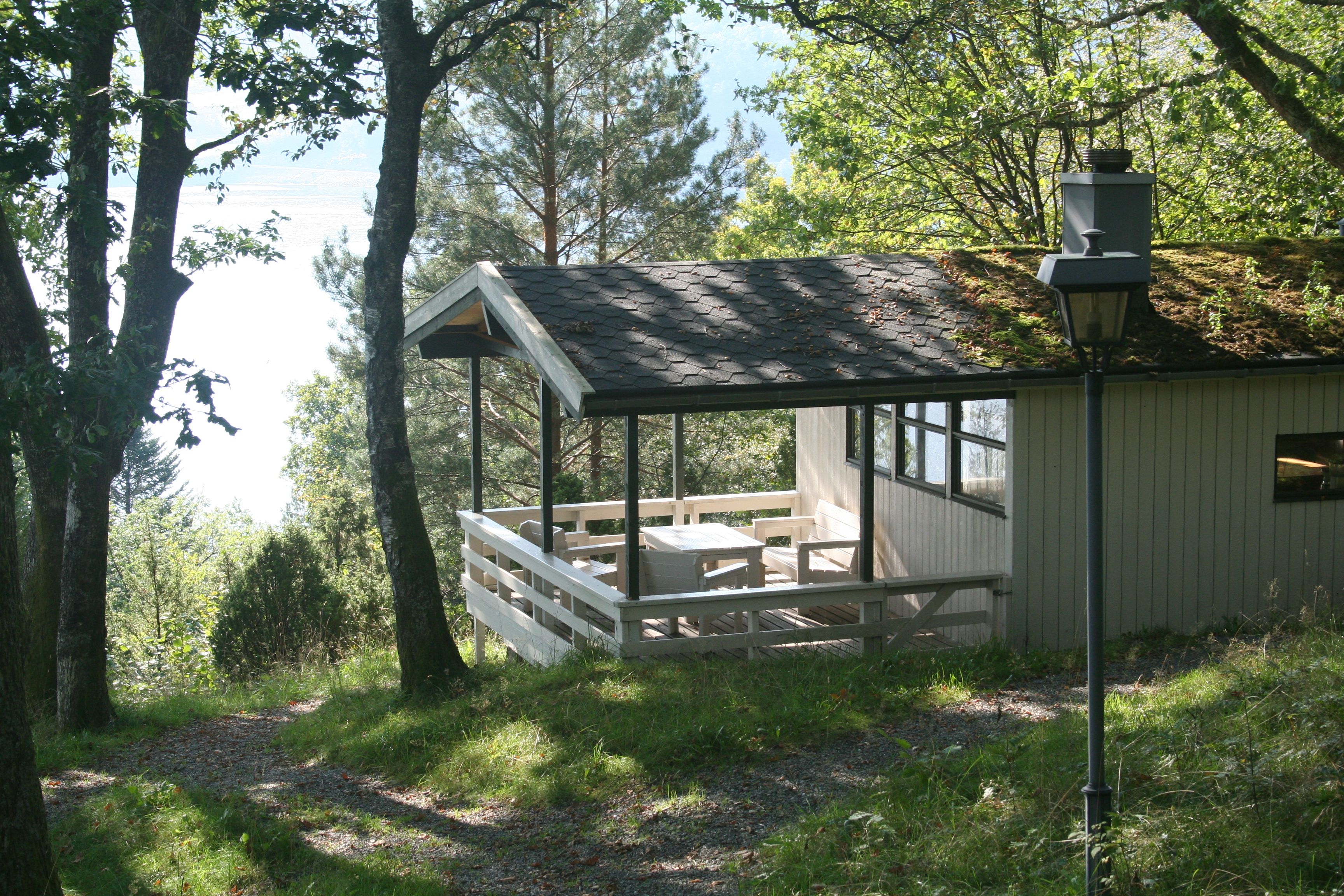 Hytte med terrasse omgitt av skog og utsikt mot fjorden.