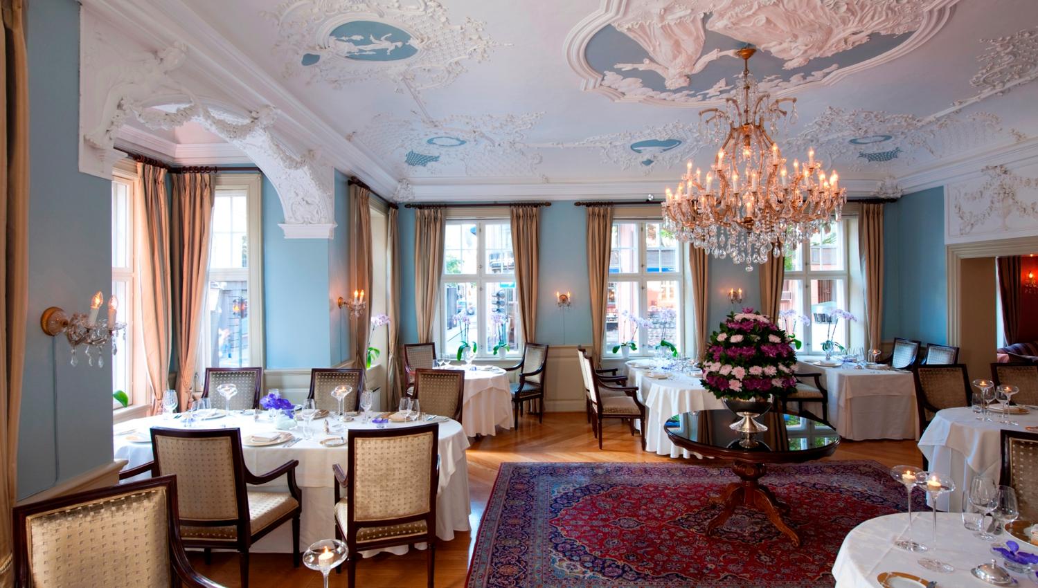 Set tables in hall with blue walls. eye crown and stucco in the ceiling.