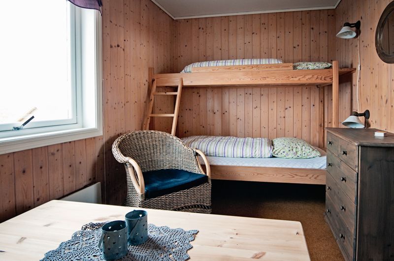 Et rom med trevegger, køyeseng, kommode, stol og bord.