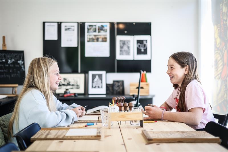 To jenter som ler og jobber med tresnitt de har fått utdelt