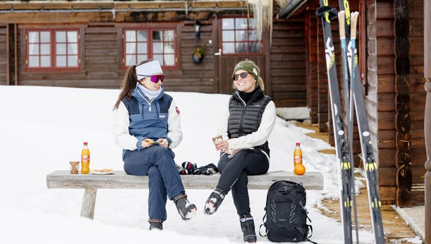 2 ladies with skis chilling outside the hut