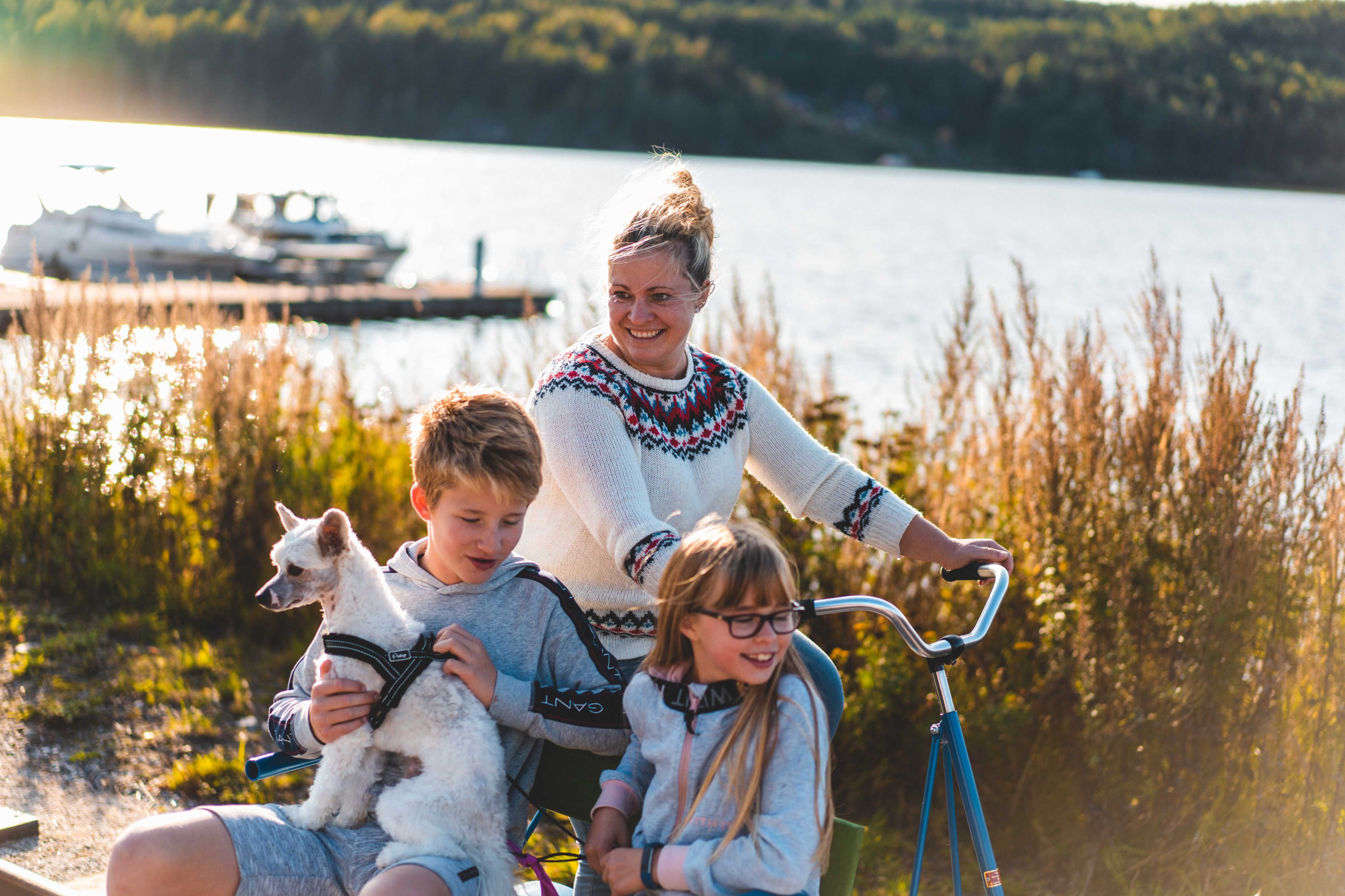 Familie sykler fresin med hund og vann i bakgrunn
