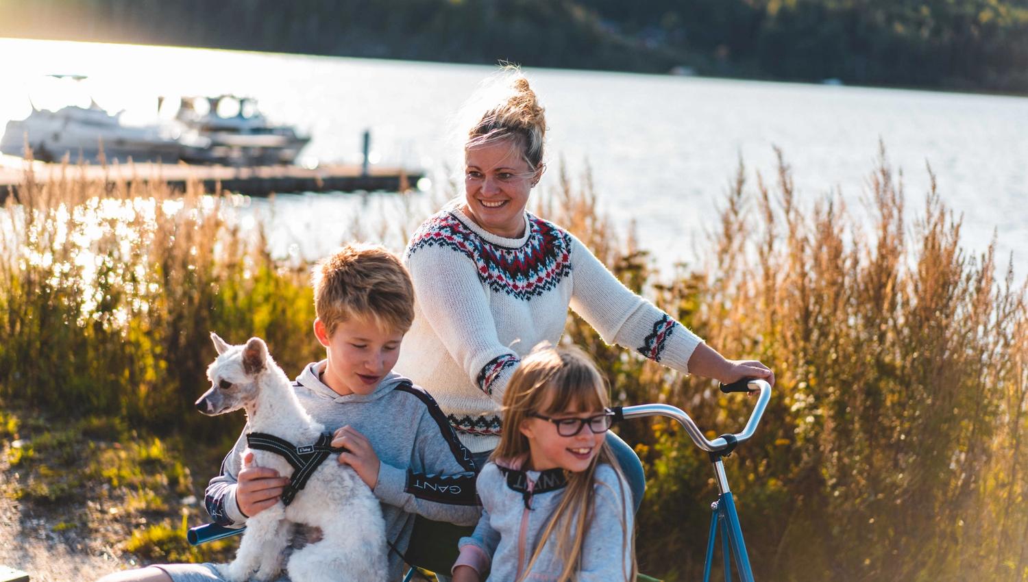 Familie sykler fresin med hund og vann i bakgrunn