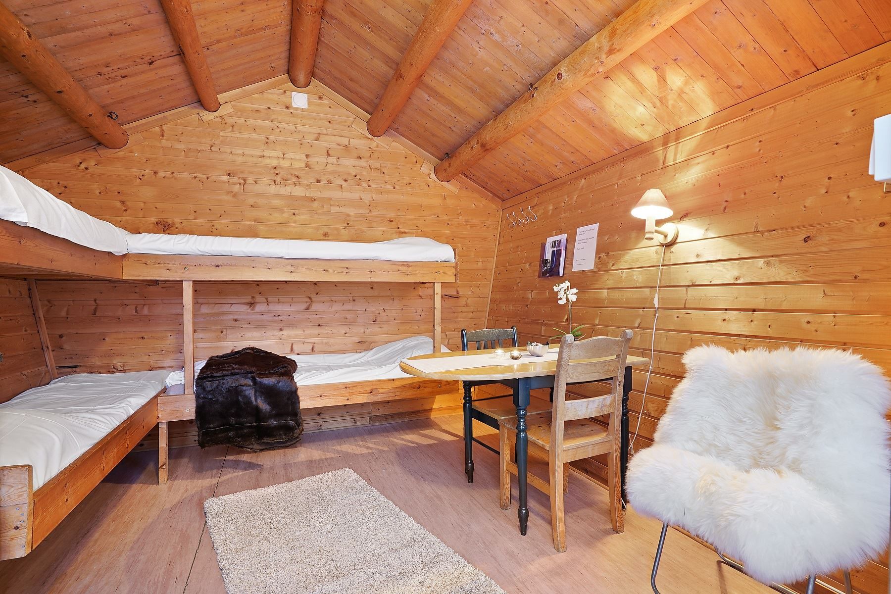 Cabin interior with bunk bed, small table, and slanted wooden ceiling