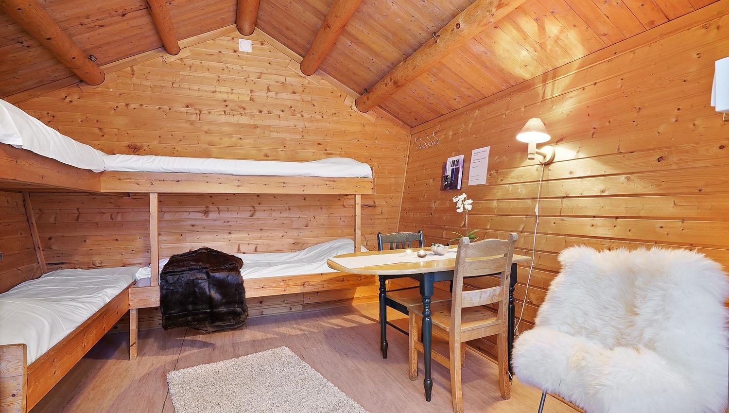 Cabin interior with bunk bed, small table, and slanted wooden ceiling