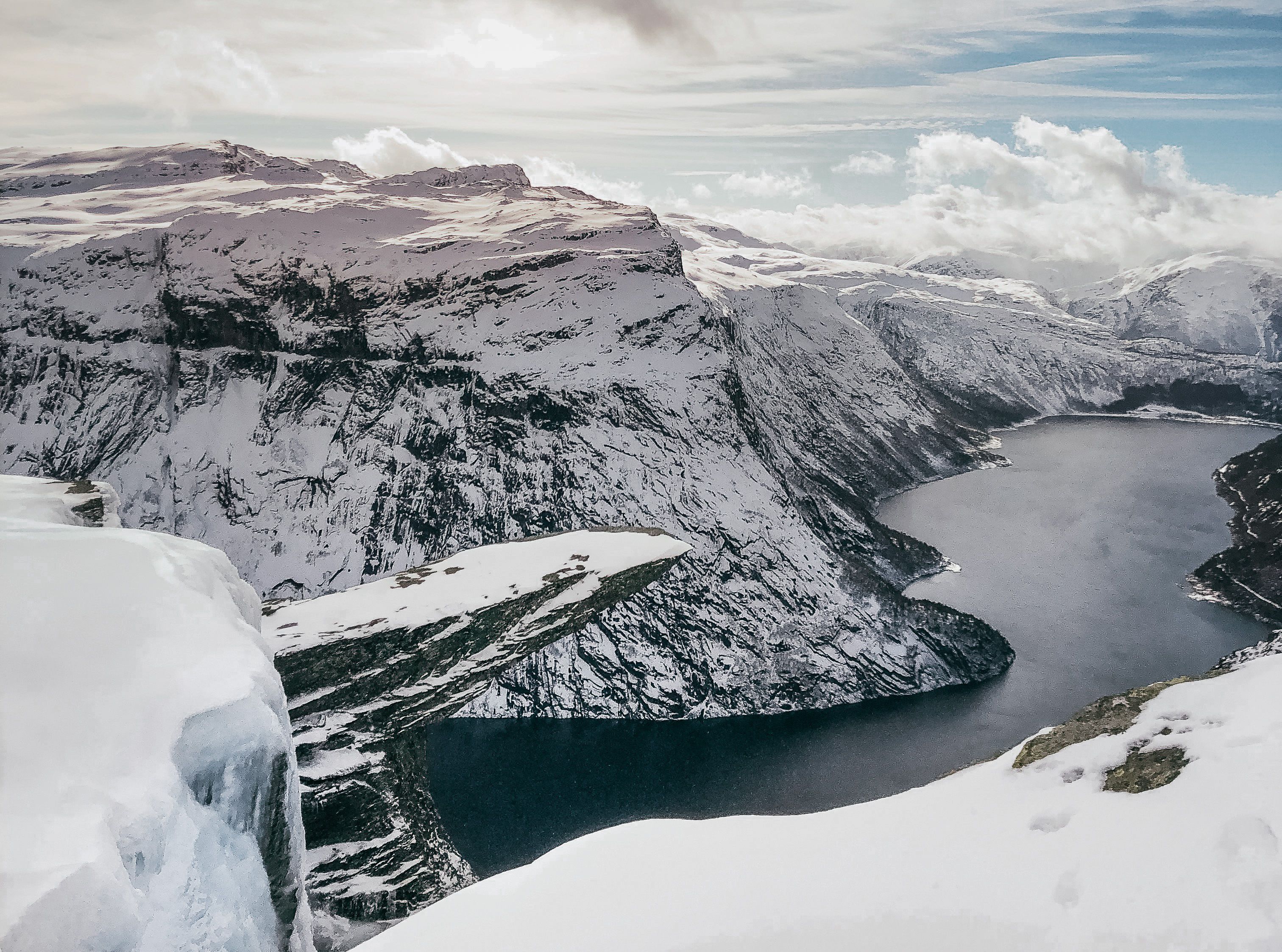 Trolltunga covered in snow and ice during winter, overlooking the fjord and surrounding peaks.