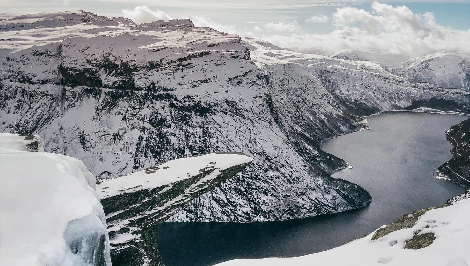 Trolltunga covered in snow and ice during winter, overlooking the fjord and surrounding peaks.
