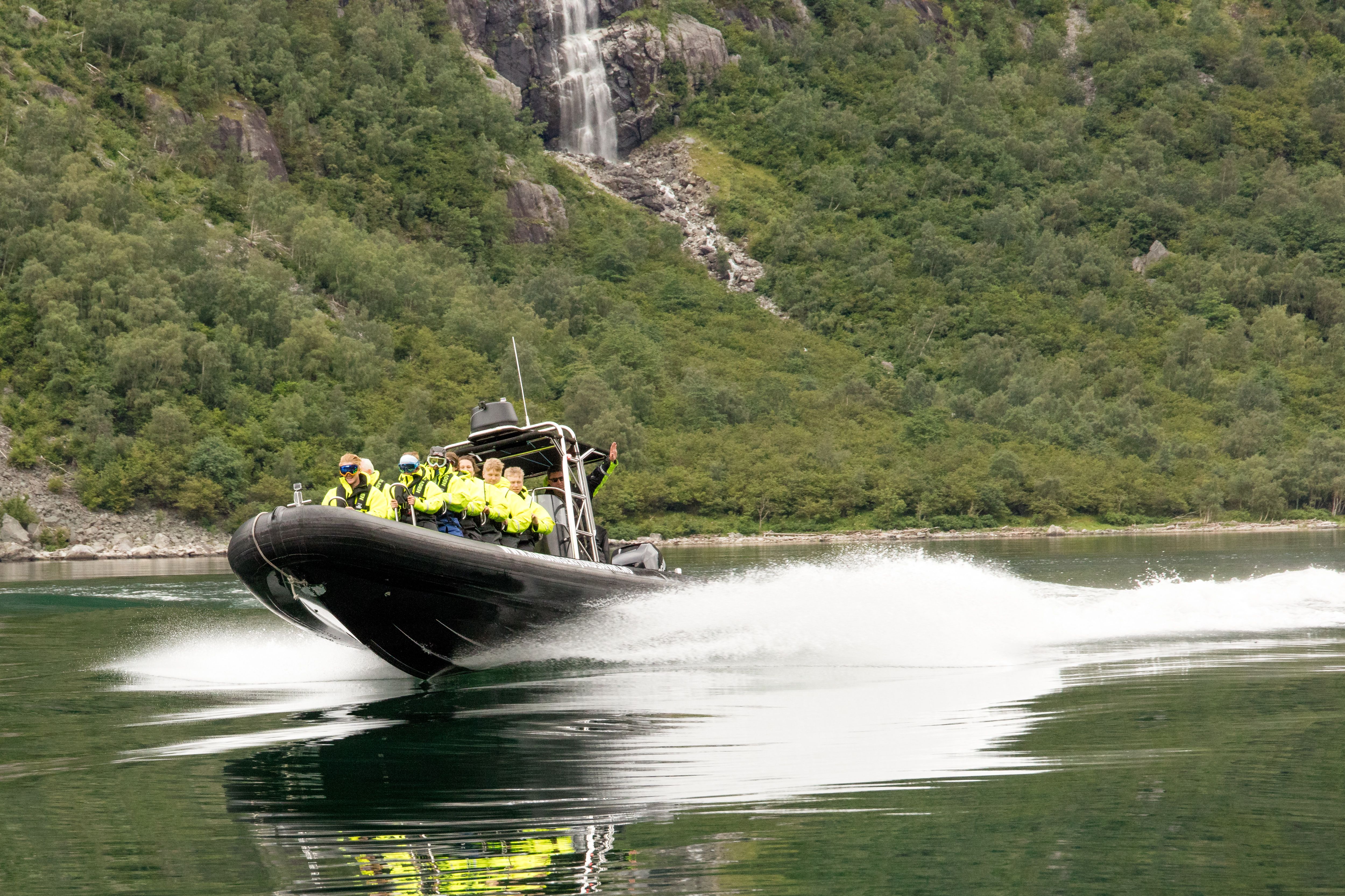 En ribbåt fylt med passasjerer i fart langs fjorden.
