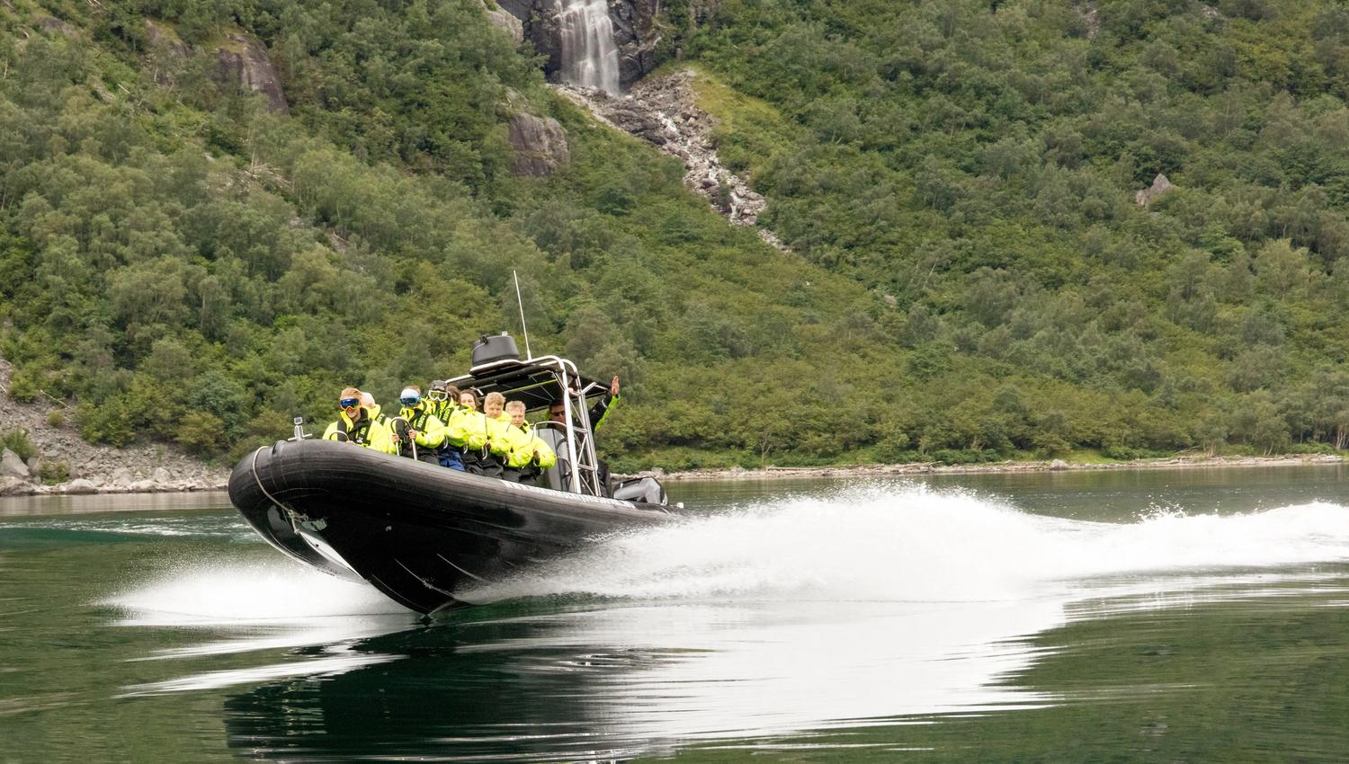 En ribbåt fylt med passasjerer i fart langs fjorden.