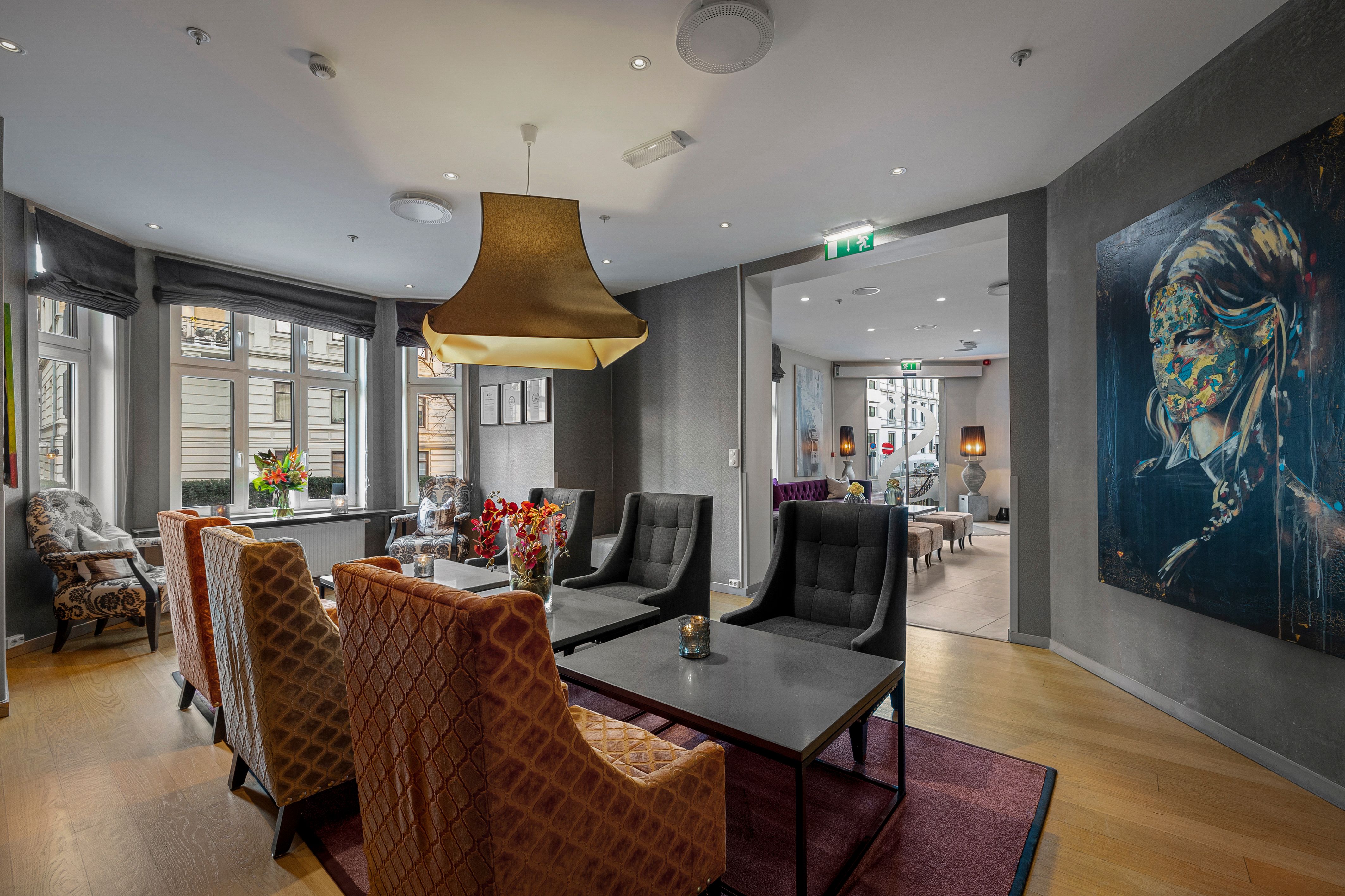 Sittegruppe med lenestoler i rødt og beige. Store vinduer. Tregulv. Kunst på Veggen. Saga Hotel Oslo. foto