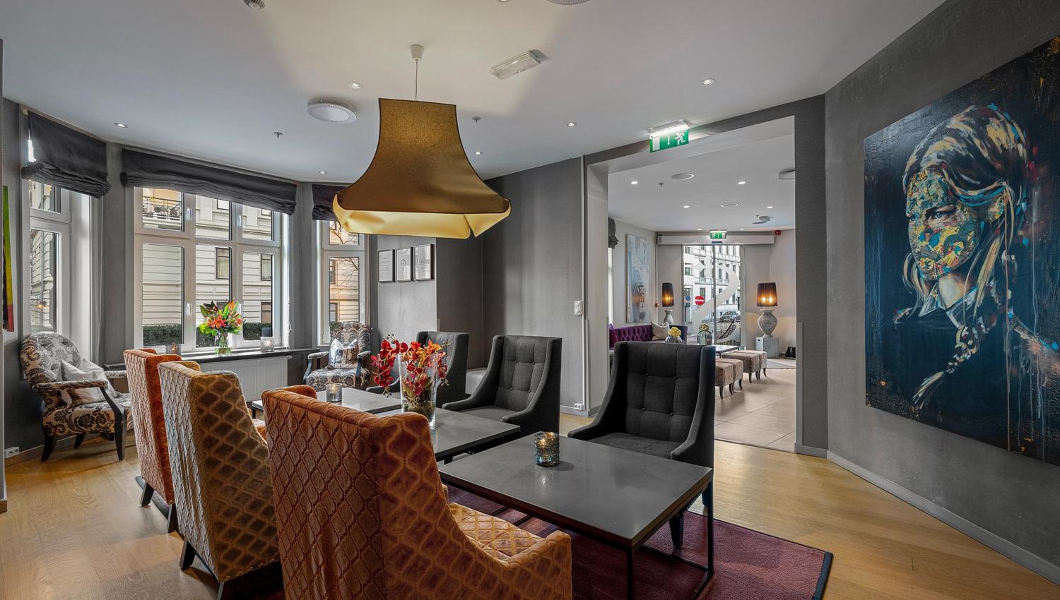 Sittegruppe med lenestoler i rødt og beige. Store vinduer. Tregulv. Kunst på Veggen. Saga Hotel Oslo. foto