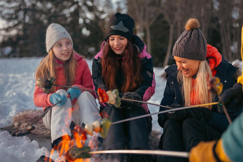 Two girls and a woman preparing food on a bonfire