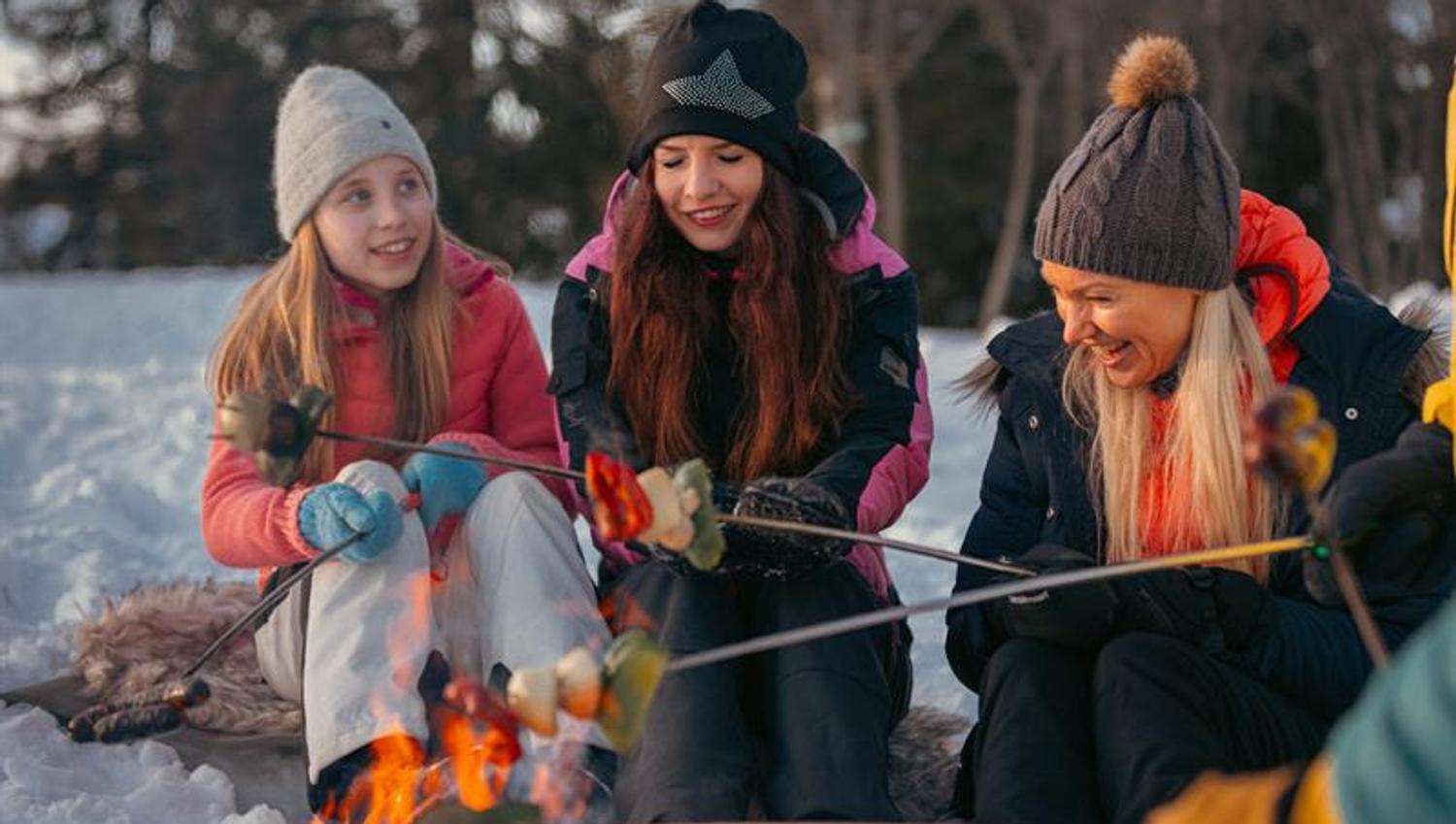 Two girls and a woman preparing food on a bonfire