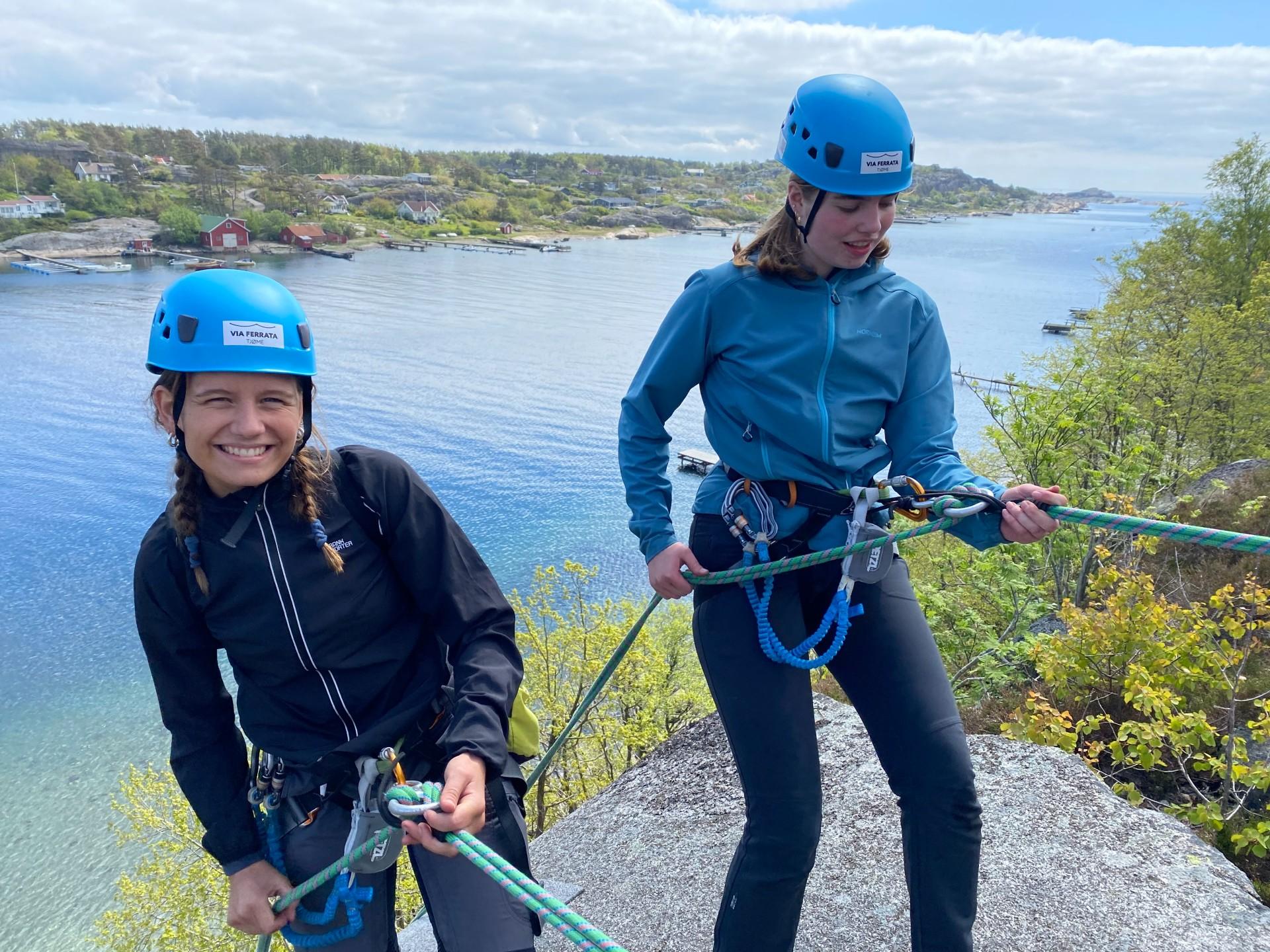 Two cheerful girls with blue helmets rappel down the mountain at Tjøme with a great view of the archipelago.