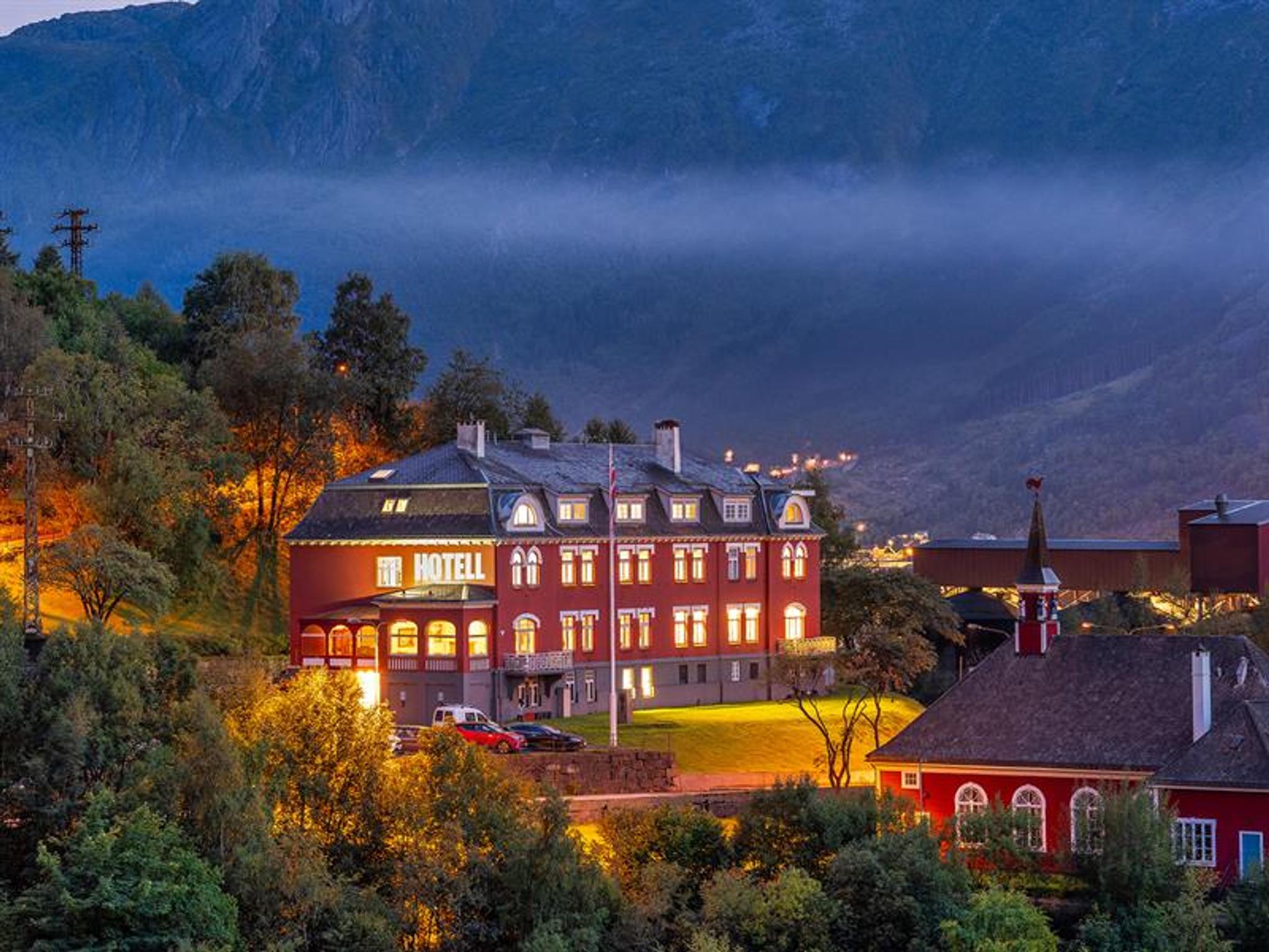 Historic Tyssedal Hotel illuminated at dusk, surrounded by mountains and the Hardangerfjord.