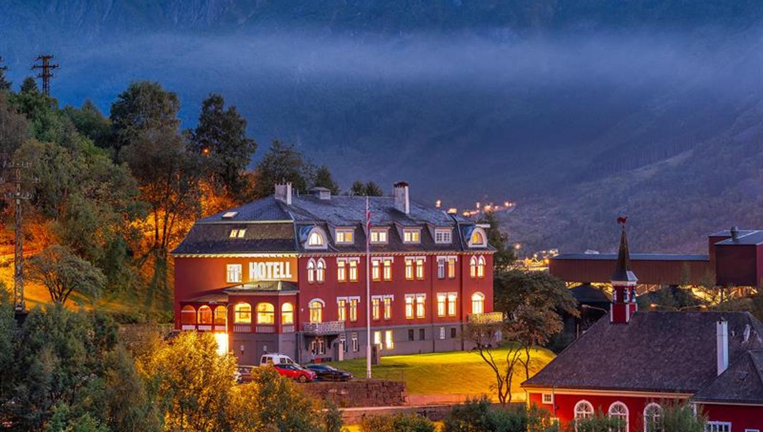 Historisk Tyssedal Hotel opplyst i kvelden, omgitt av fjell og Hardangerfjorden.