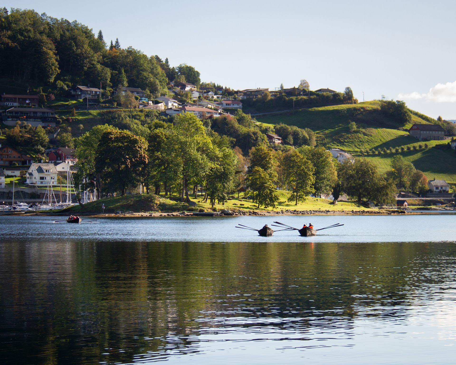 Rowboats on the fjord with green hills and houses in the background near Hardanger Maritime Center.