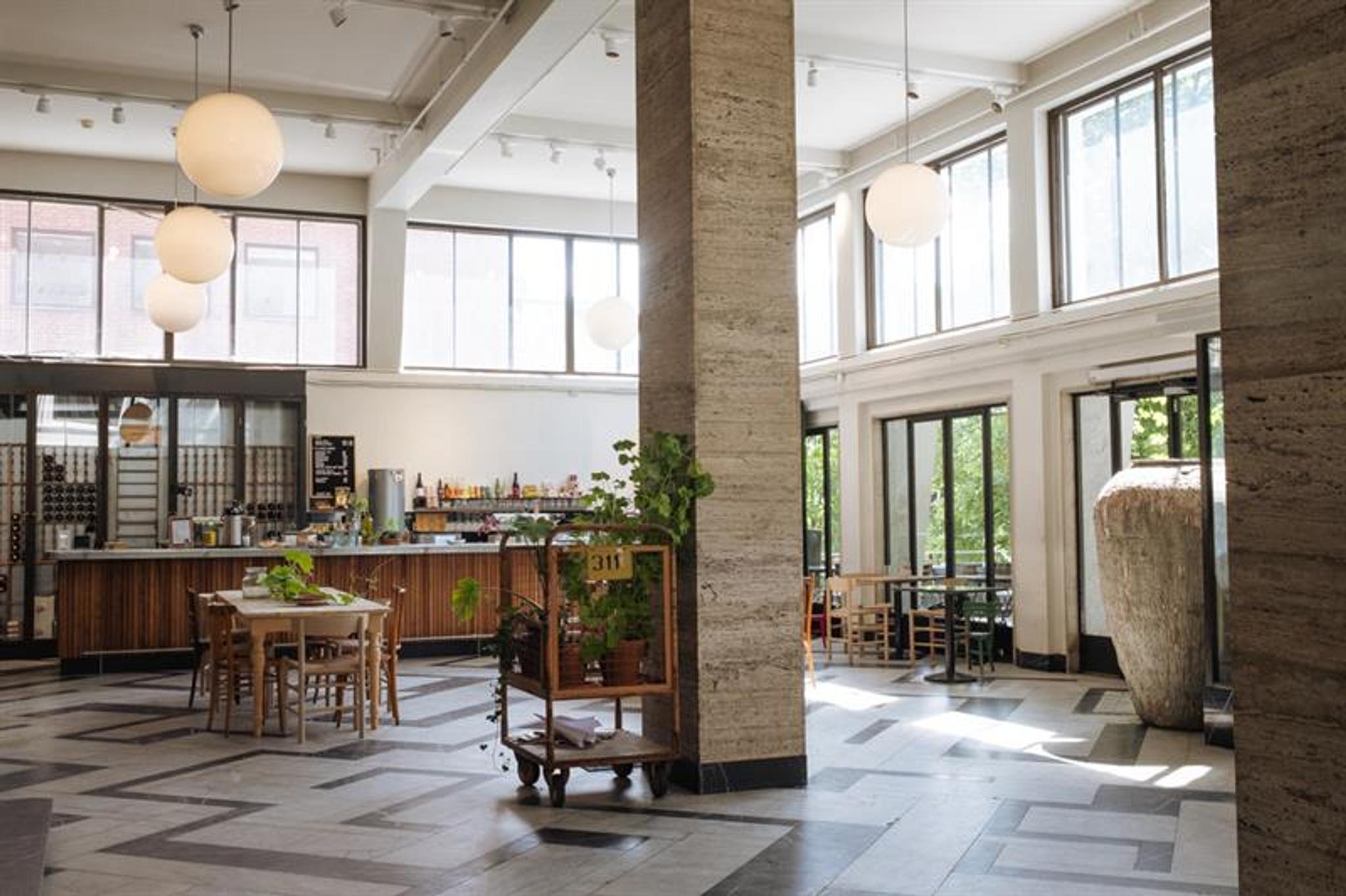 Café interior with a high ceiling, square pillars, globe-shaped ceiling lamps, a bar counter, square tables, and large windows