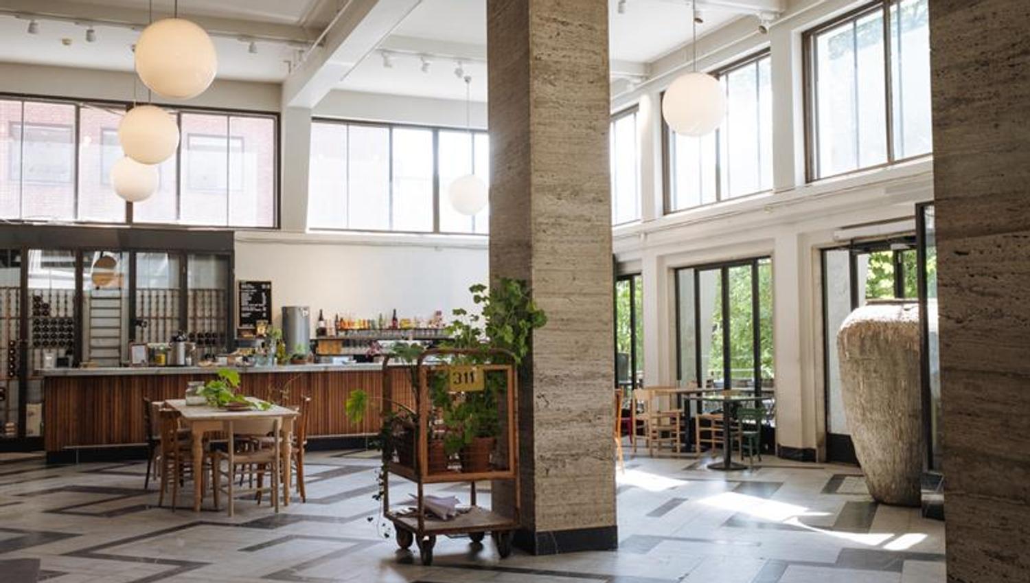 Café interior with a high ceiling, square pillars, globe-shaped ceiling lamps, a bar counter, square tables, and large windows