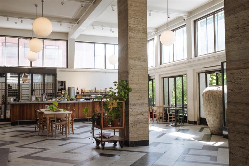Café interior with a high ceiling, square pillars, globe-shaped ceiling lamps, a bar counter, square tables, and large windows
