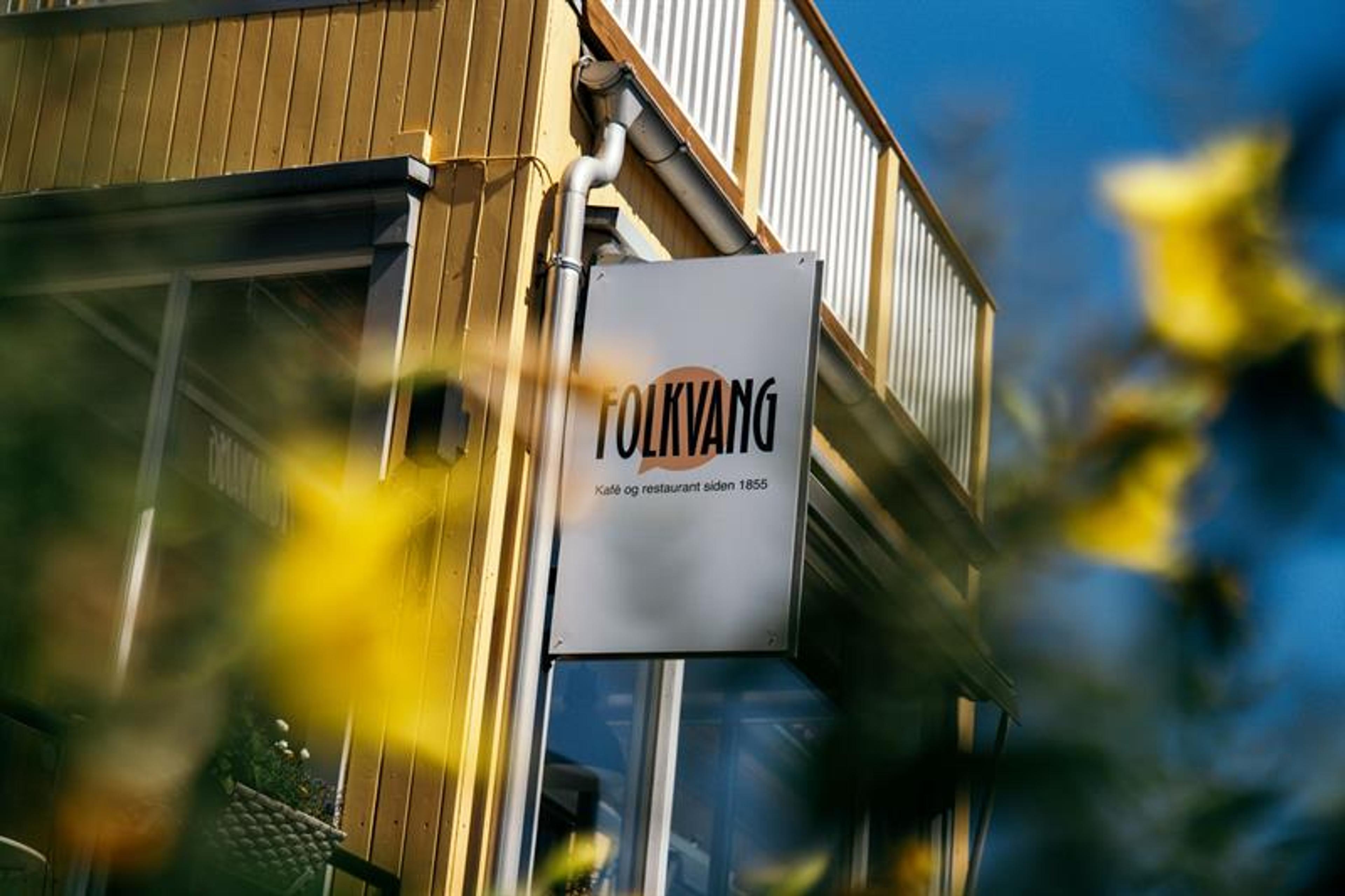 Skiltet til Folkvang – kafé og restaurant siden 1855 – montert på byggets fasade omgitt av blomster.