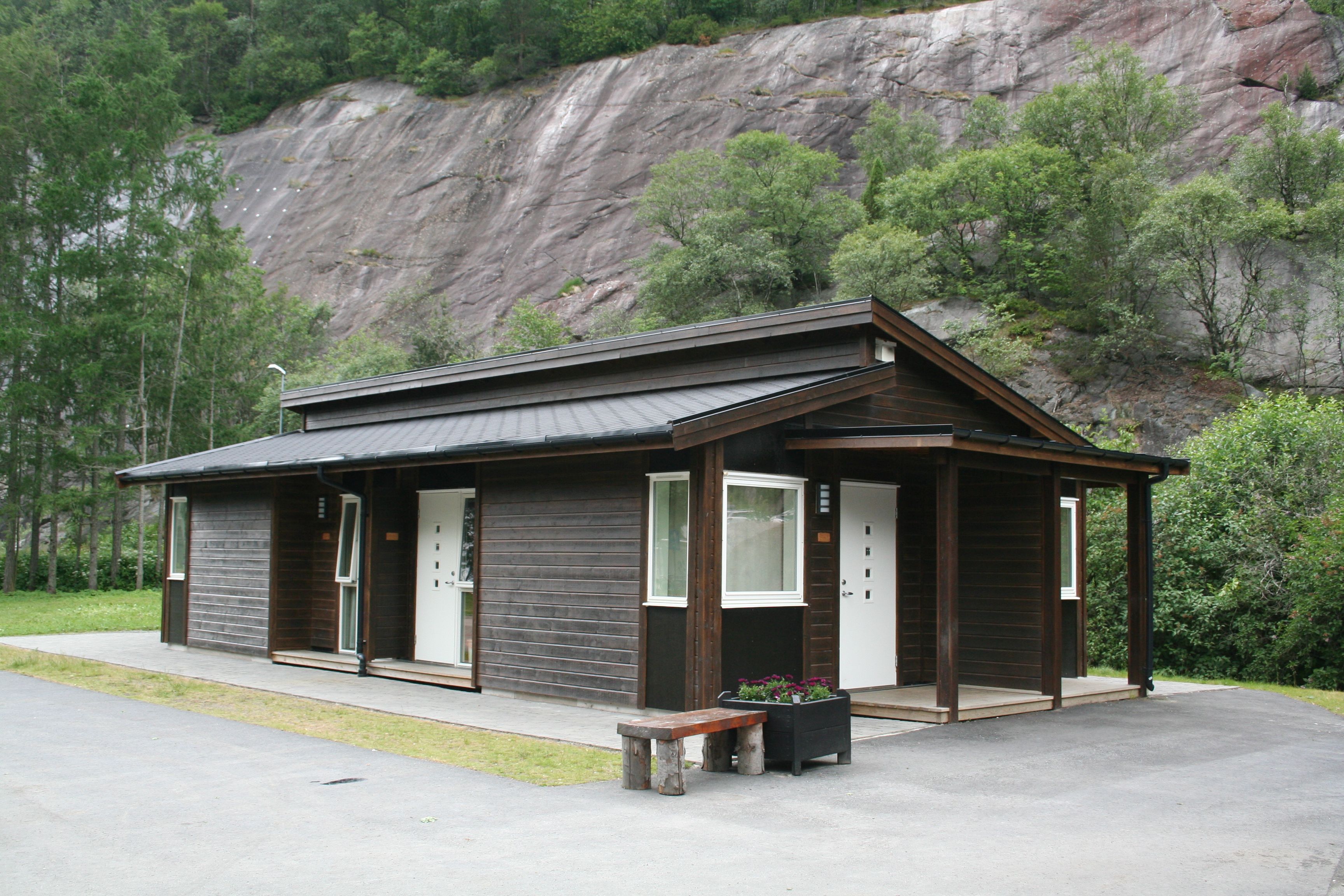 Moderne campinghytter i tre med bratte fjellsider i bakgrunnen.