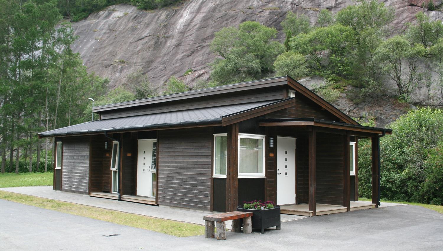 Moderne campinghytter i tre med bratte fjellsider i bakgrunnen.