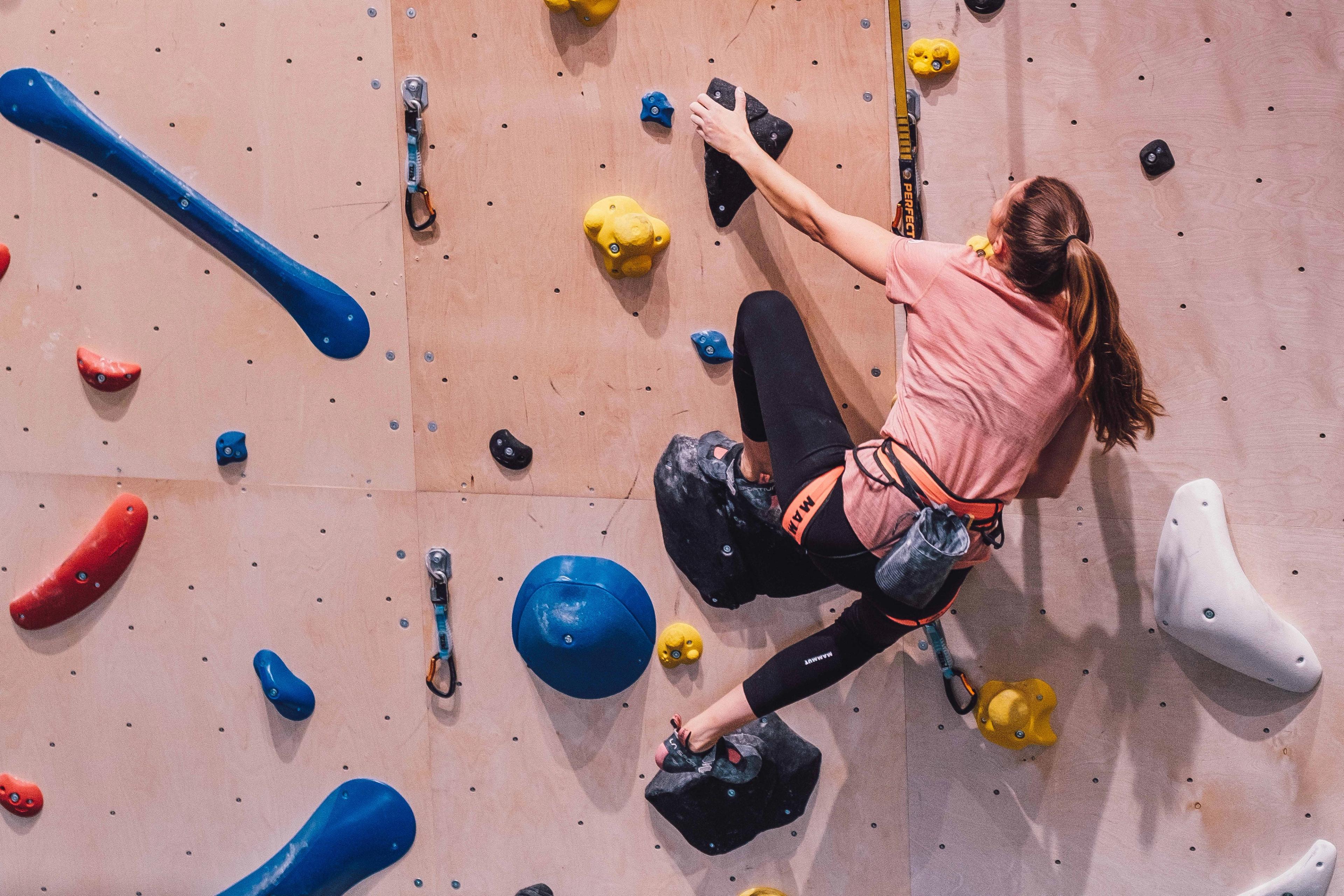 Jente som henger i klatresele i klatrevegg