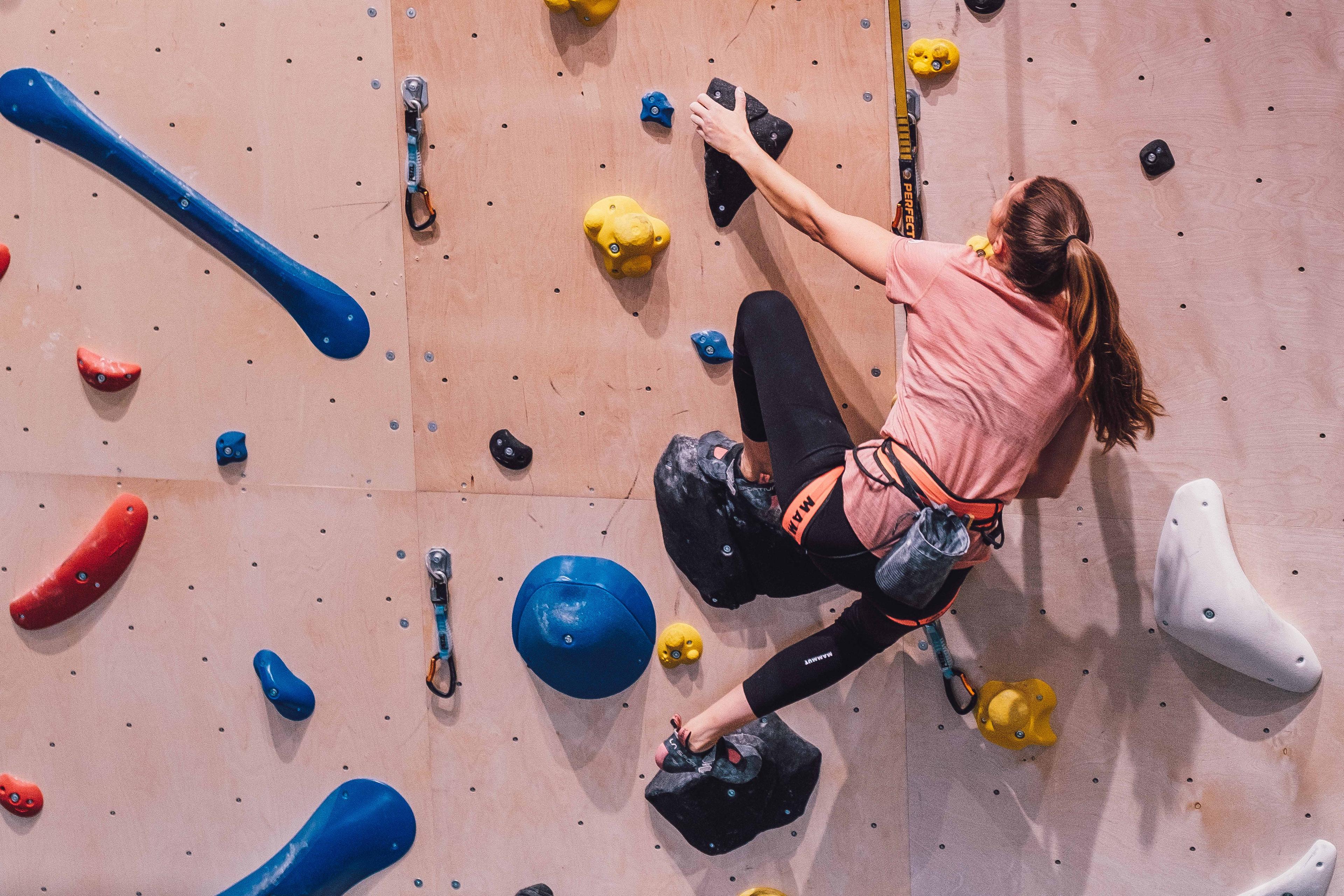 Jente som henger i klatresele i klatrevegg