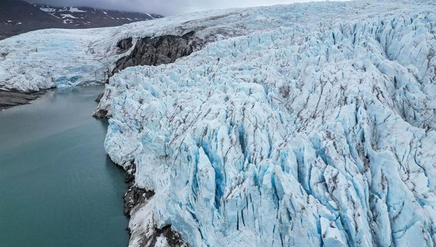 Dronebilde av blå isbre og smeltevann.