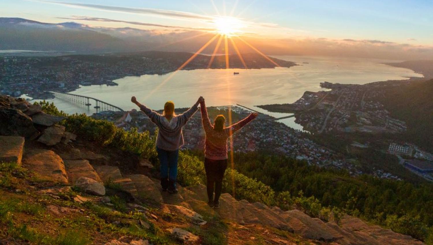 To personer holder hender og ser mot midnattsola fra Sherpatrappa i Tromsø