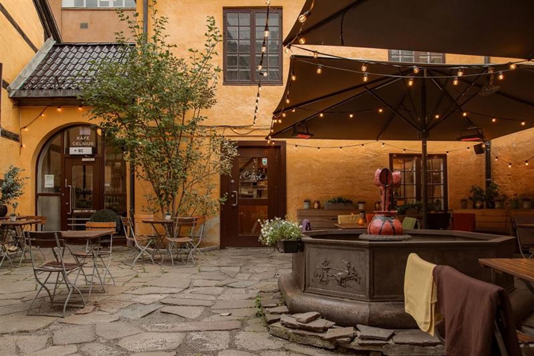 Charming outdoor seating in a cobbled courtyard with parasols, string lights and historic buildings surrounding the area.
