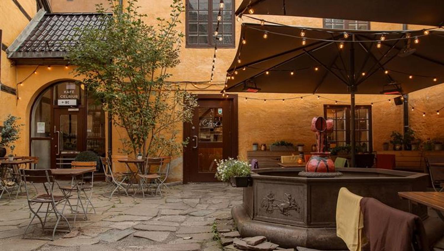 Charming outdoor seating in a cobbled courtyard with parasols, string lights and historic buildings surrounding the area.