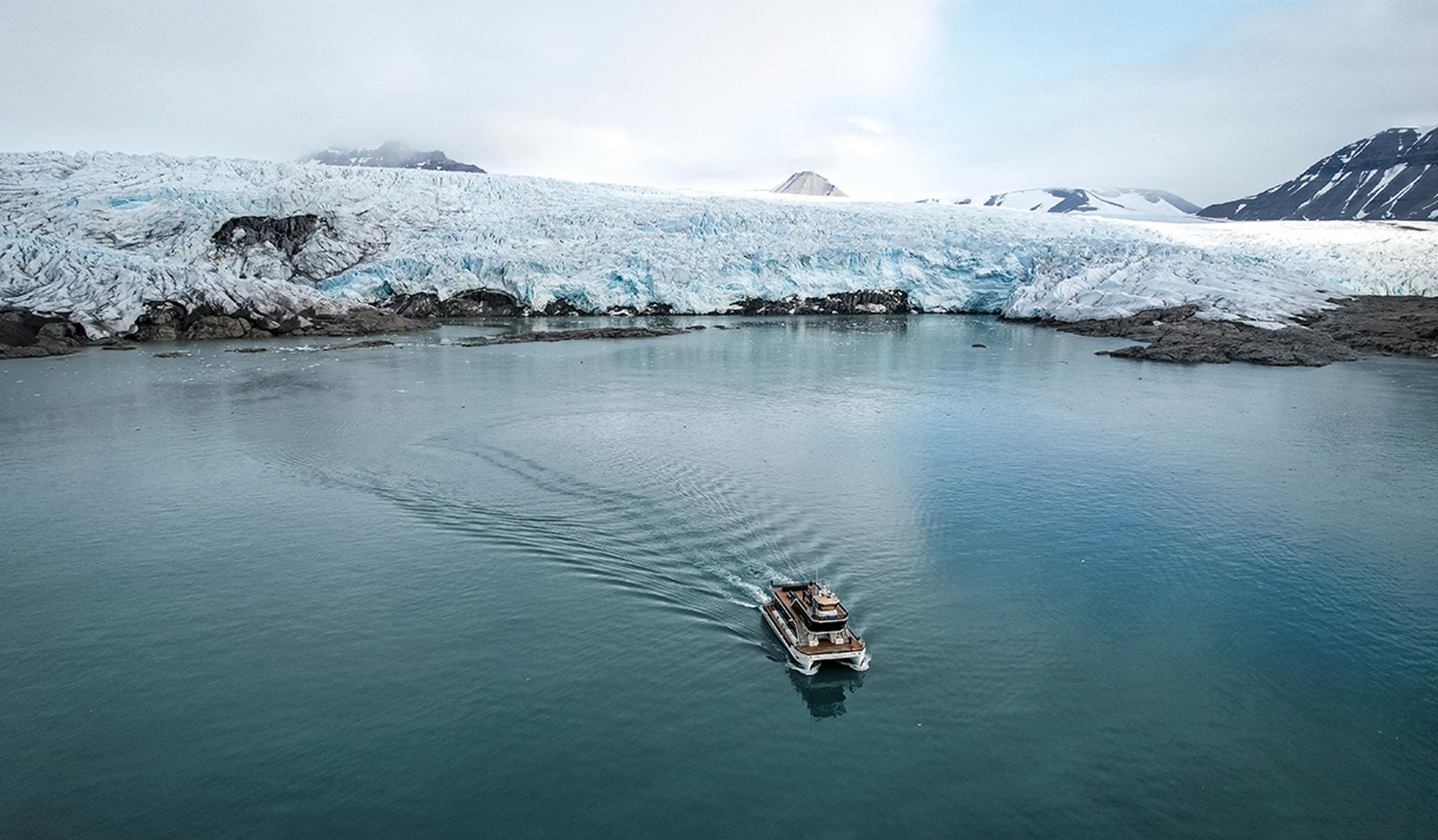 A boat sailing on a fjord in the foreground with a glacier front and mountains surrounding a bay in the background