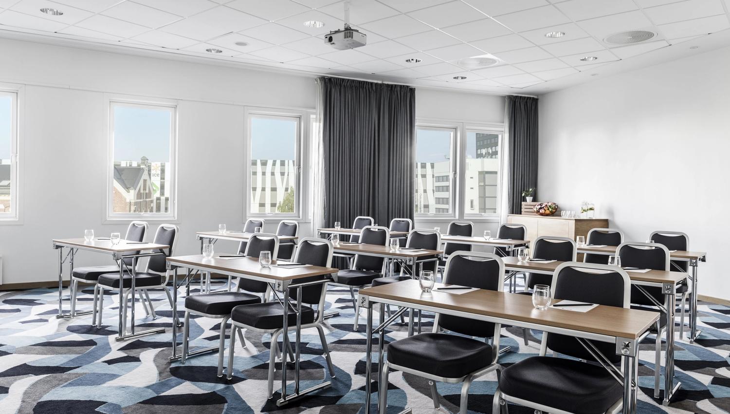 Classroom setup in a meeting room. patterned carpet, two seats per table. Photo