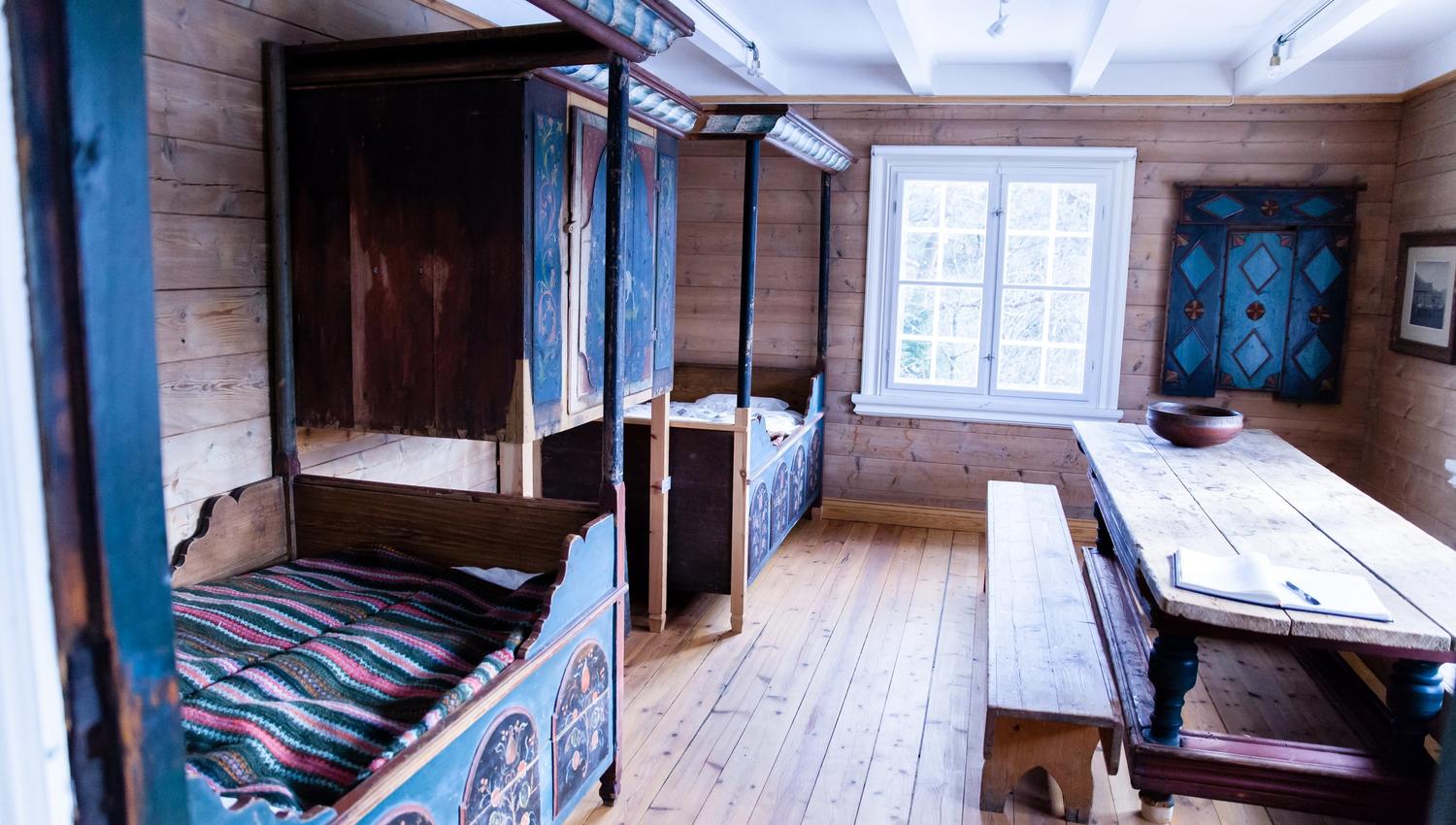 Marnardal Museum og Mjålandsstova, to senger med overskap midt i. Malt i blått med detaljer. Stort bord med benker vedsiden av
