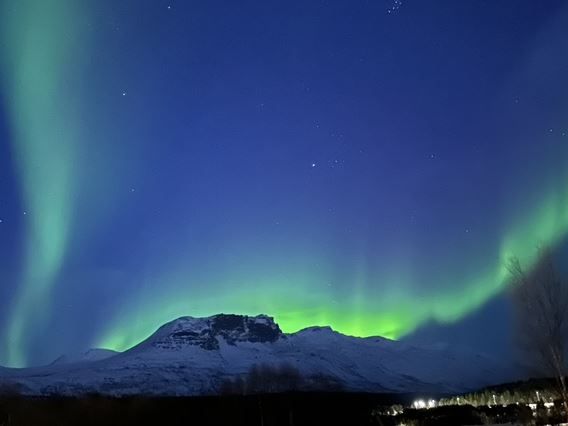Northern Lights form streak behind the mountains