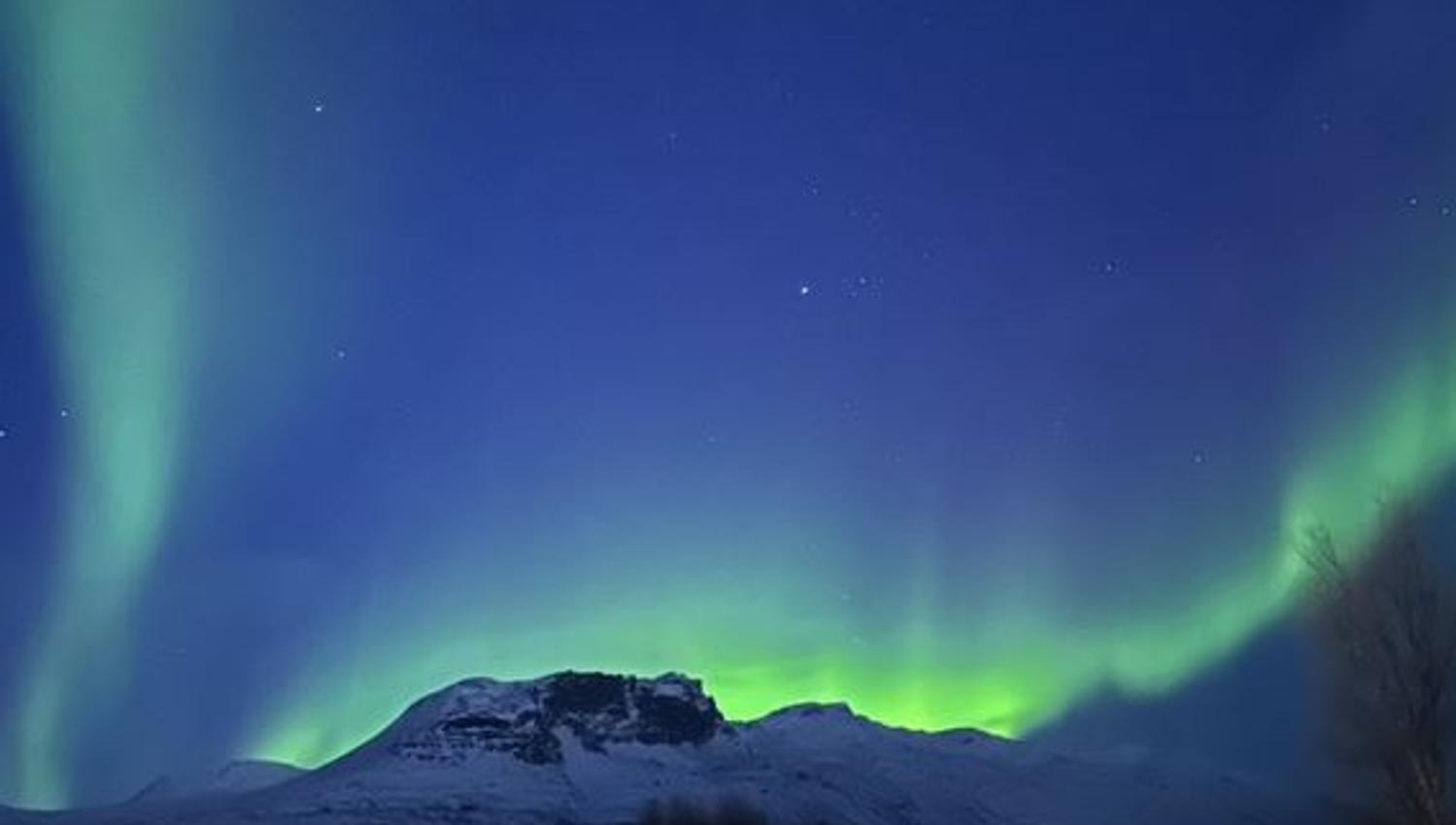 Northern Lights form streak behind the mountains