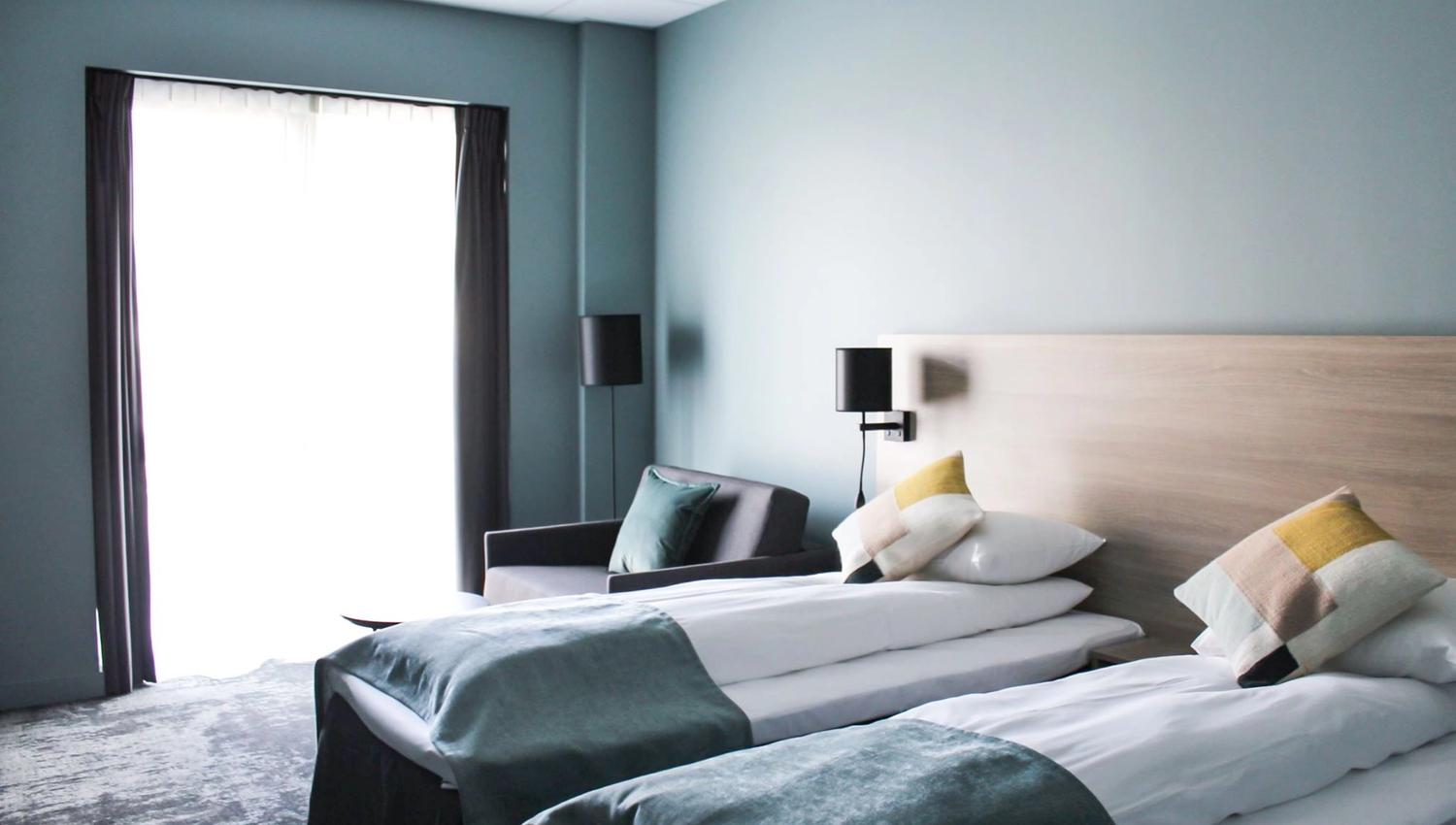 Lyst hotellrom med to enkeltsenger og moderne innreiing.