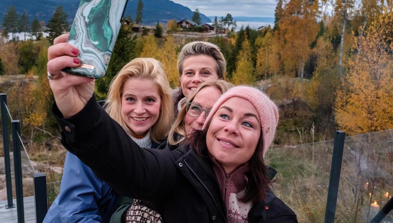 Personer tar en selfie i et skogsområde med høstfarger.