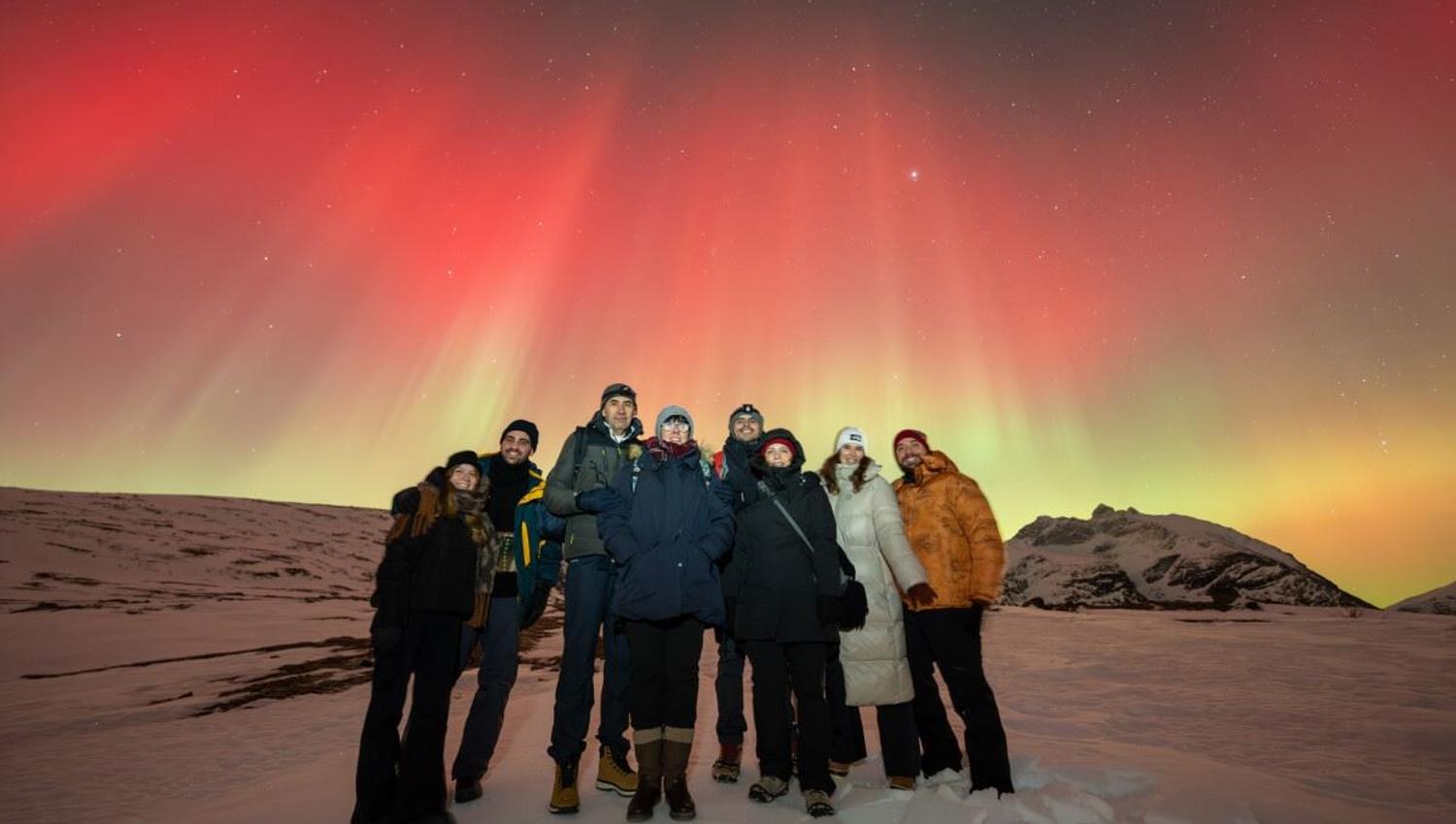 Rødt nordlys knitrer bak en gruppe med gjester