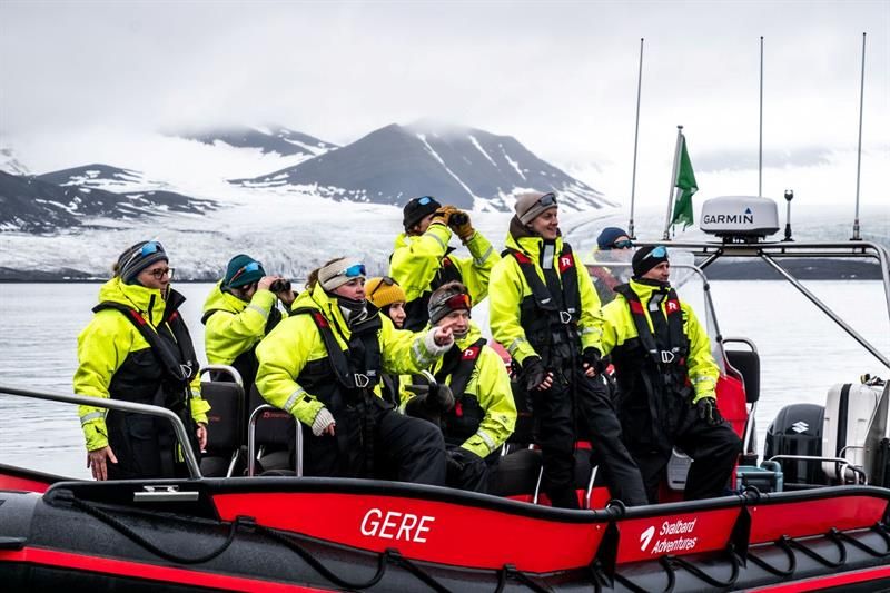 Turgruppe i gule overlevelsesdrakter på RIB-båt, speider mot isbre og fjell.