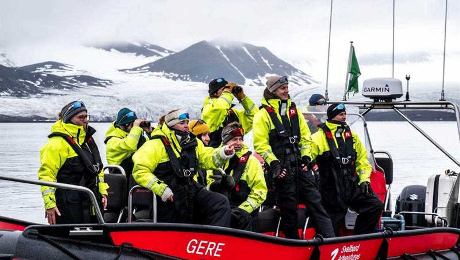 Turgruppe i gule overlevelsesdrakter på RIB-båt, speider mot isbre og fjell.