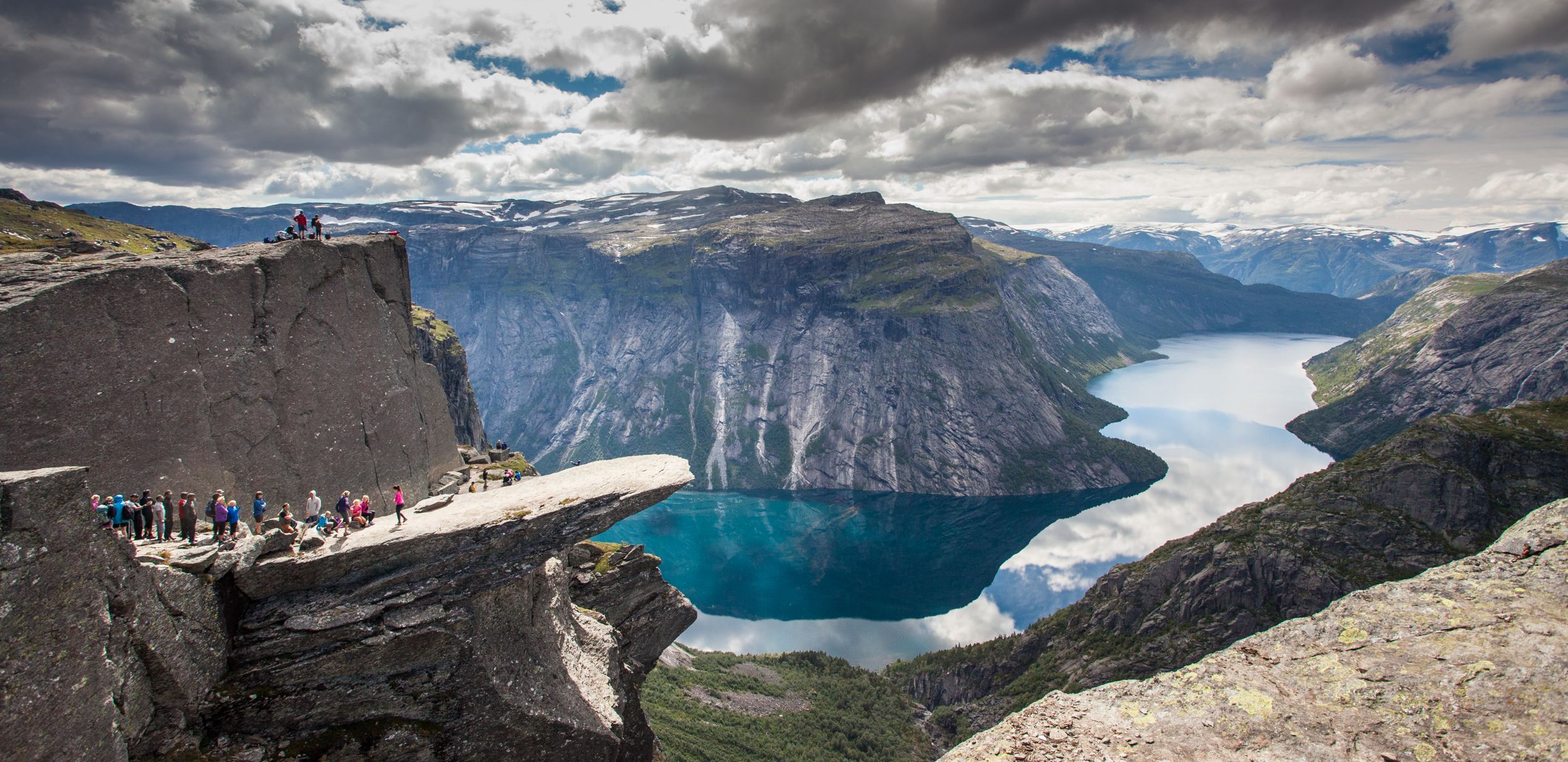 Spektakulær utsikt frå Trolltunga, eit av Noregs mest ikoniske fjellformasjonar, med blått vatn og dramatiske fjell i bakgrunnen.