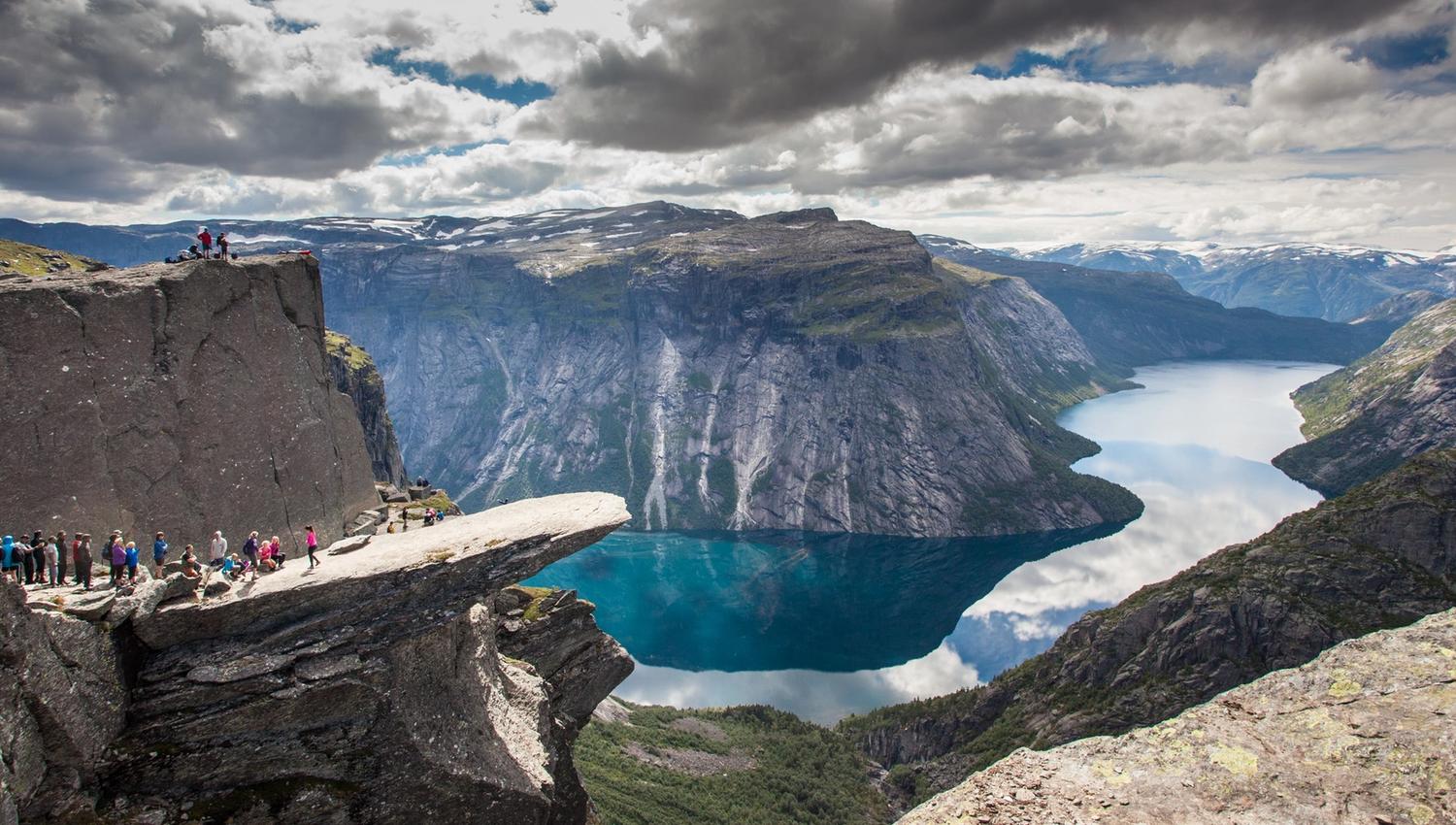 Spektakulær utsikt frå Trolltunga, eit av Noregs mest ikoniske fjellformasjonar, med blått vatn og dramatiske fjell i bakgrunnen.