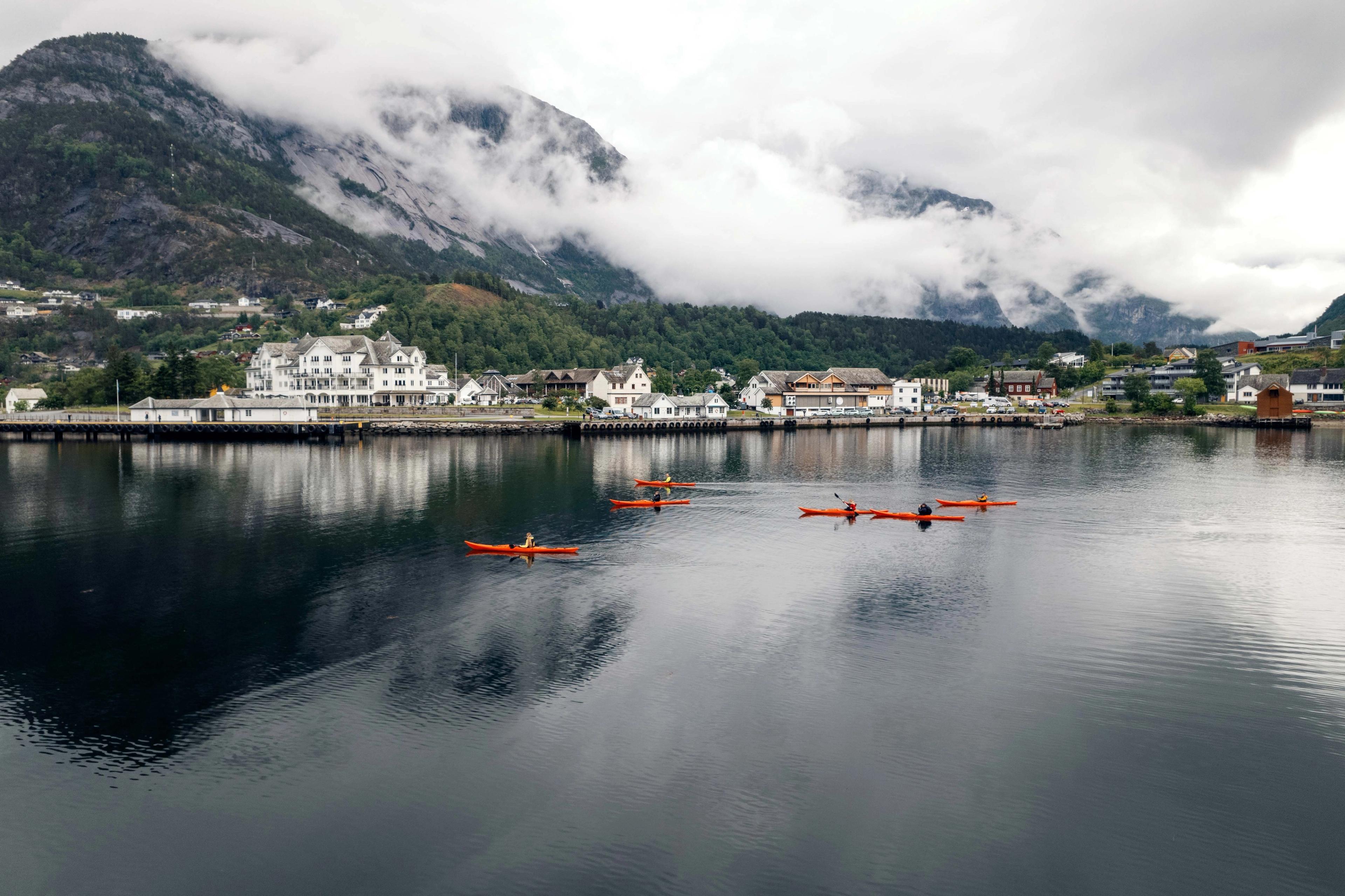 Flere røde kajakker på fjorden, med Eidfjord sentrum i bakgrunnen.