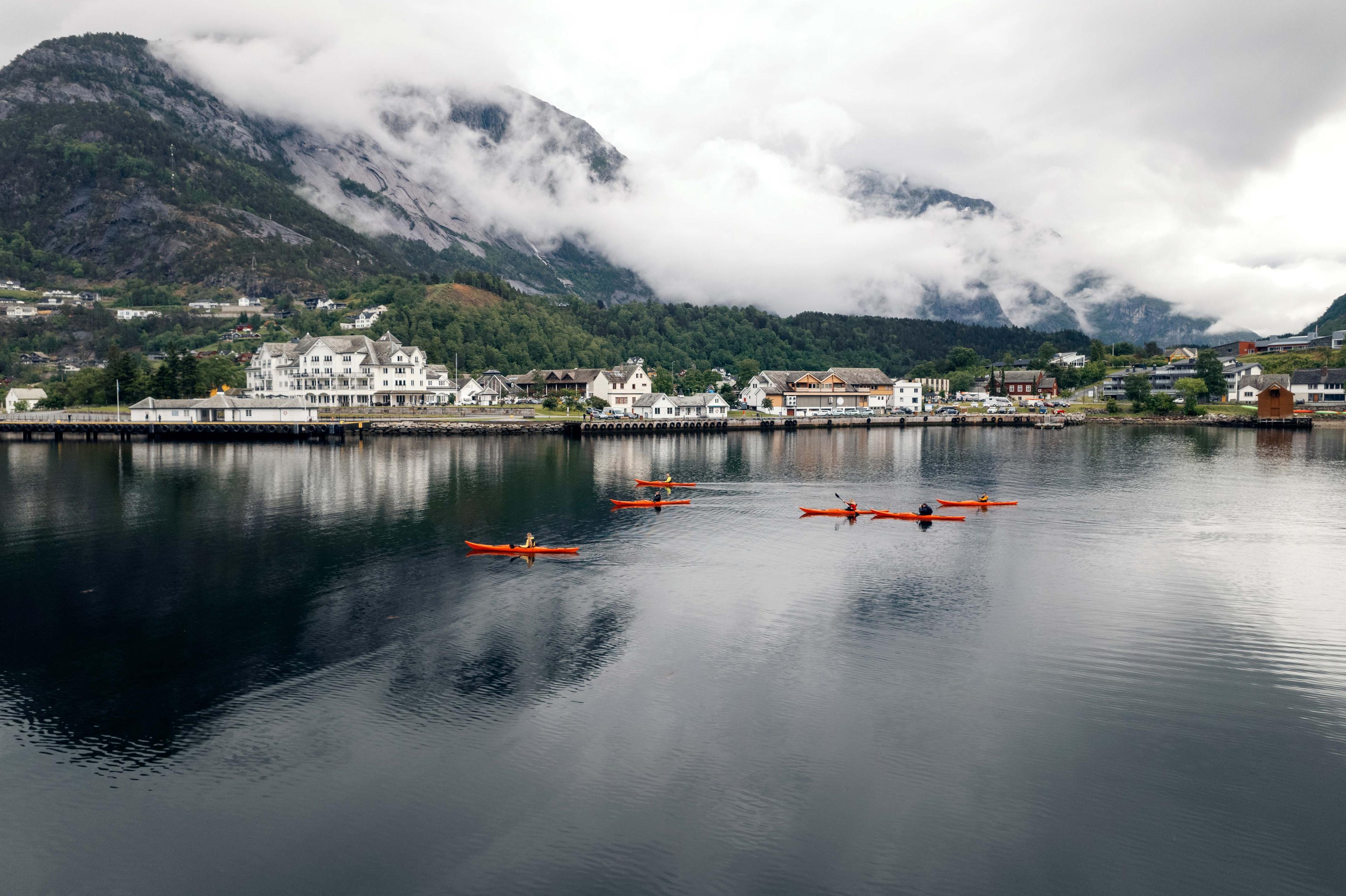 Flere røde kajakker på fjorden, med Eidfjord sentrum i bakgrunnen.